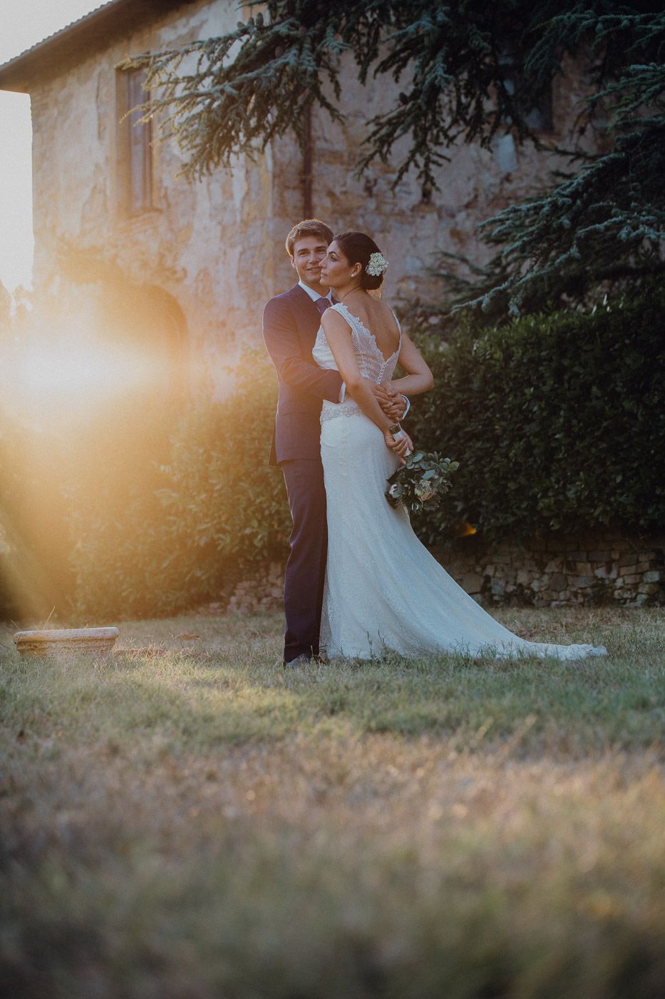 Romantic bride and groom embrace in golden sunset light outside rustic stone villa at wedding. Tuscany Villa Catignano