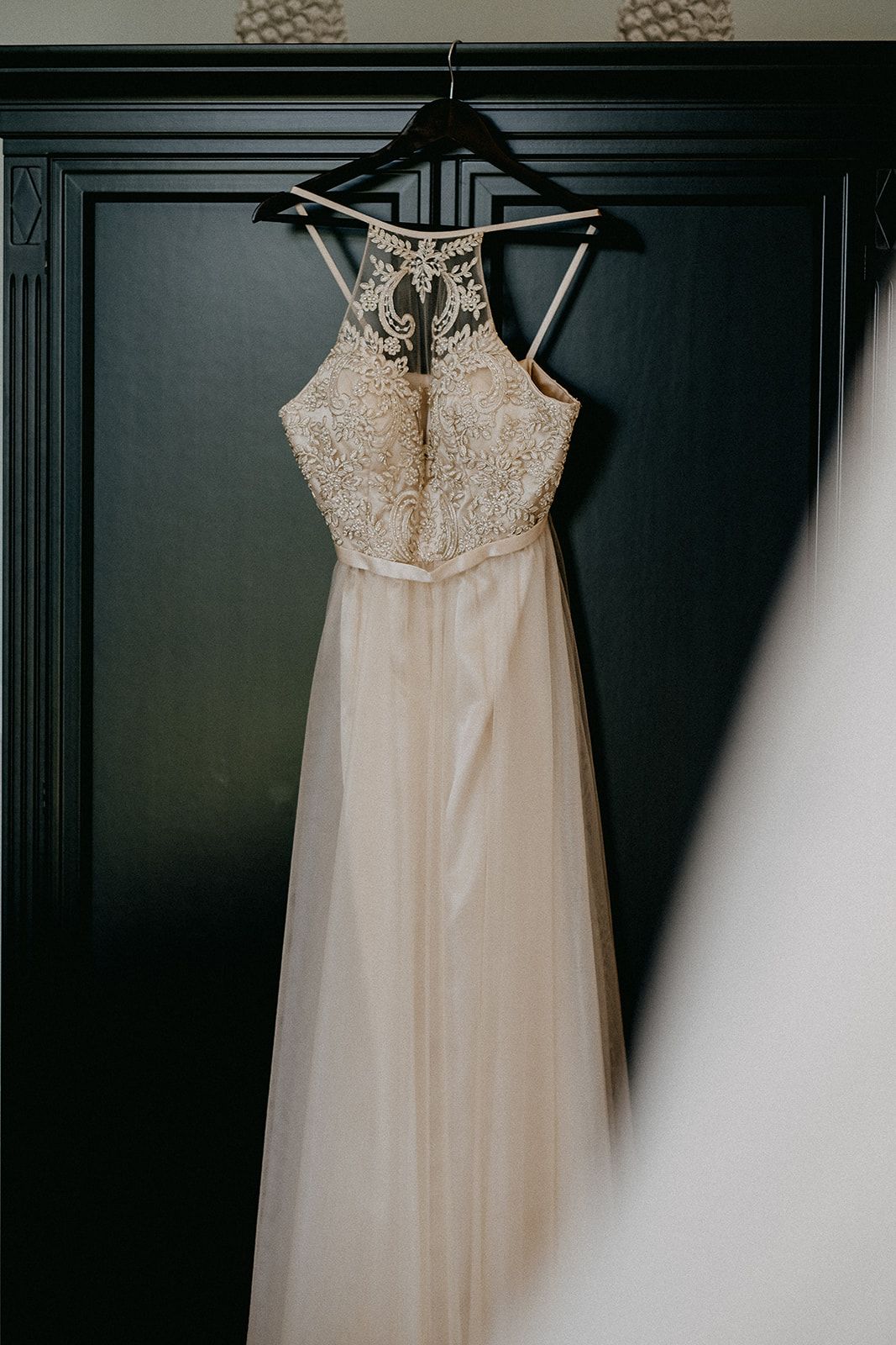 Elegant halter-neck wedding gown with intricate lace bodice hanging on dark wardrobe door.