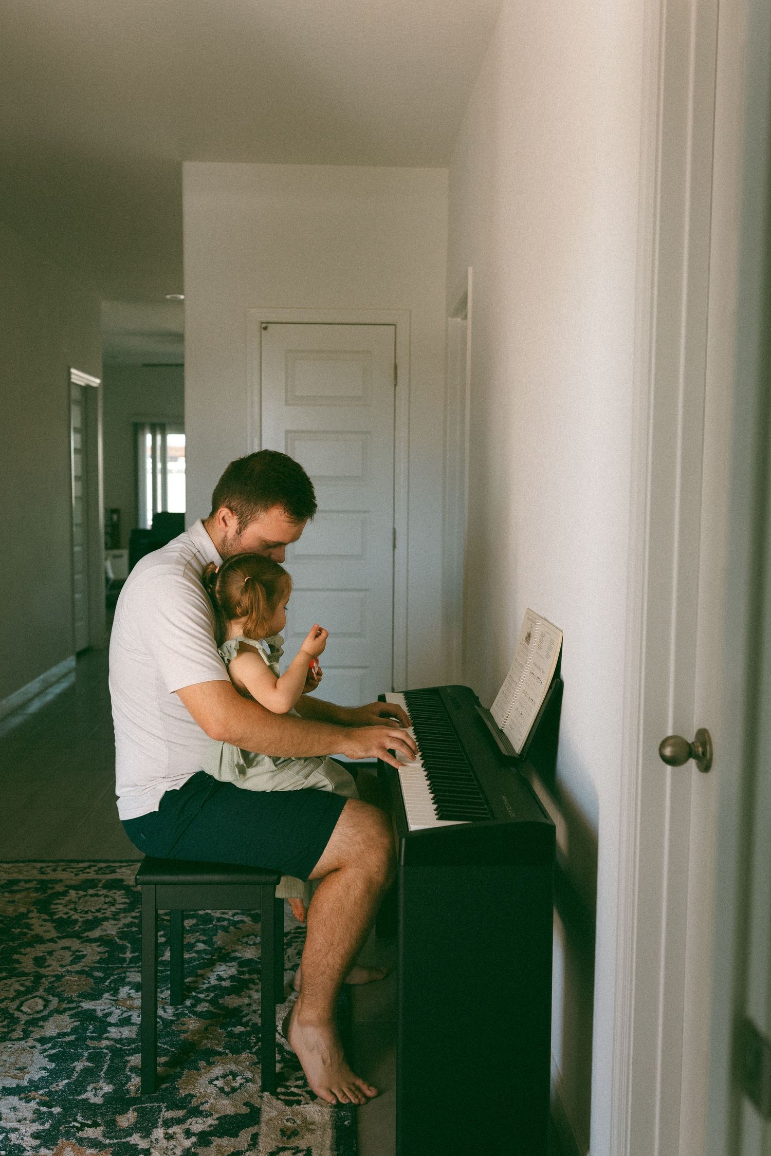 father holding daughter on lap while they play the piano