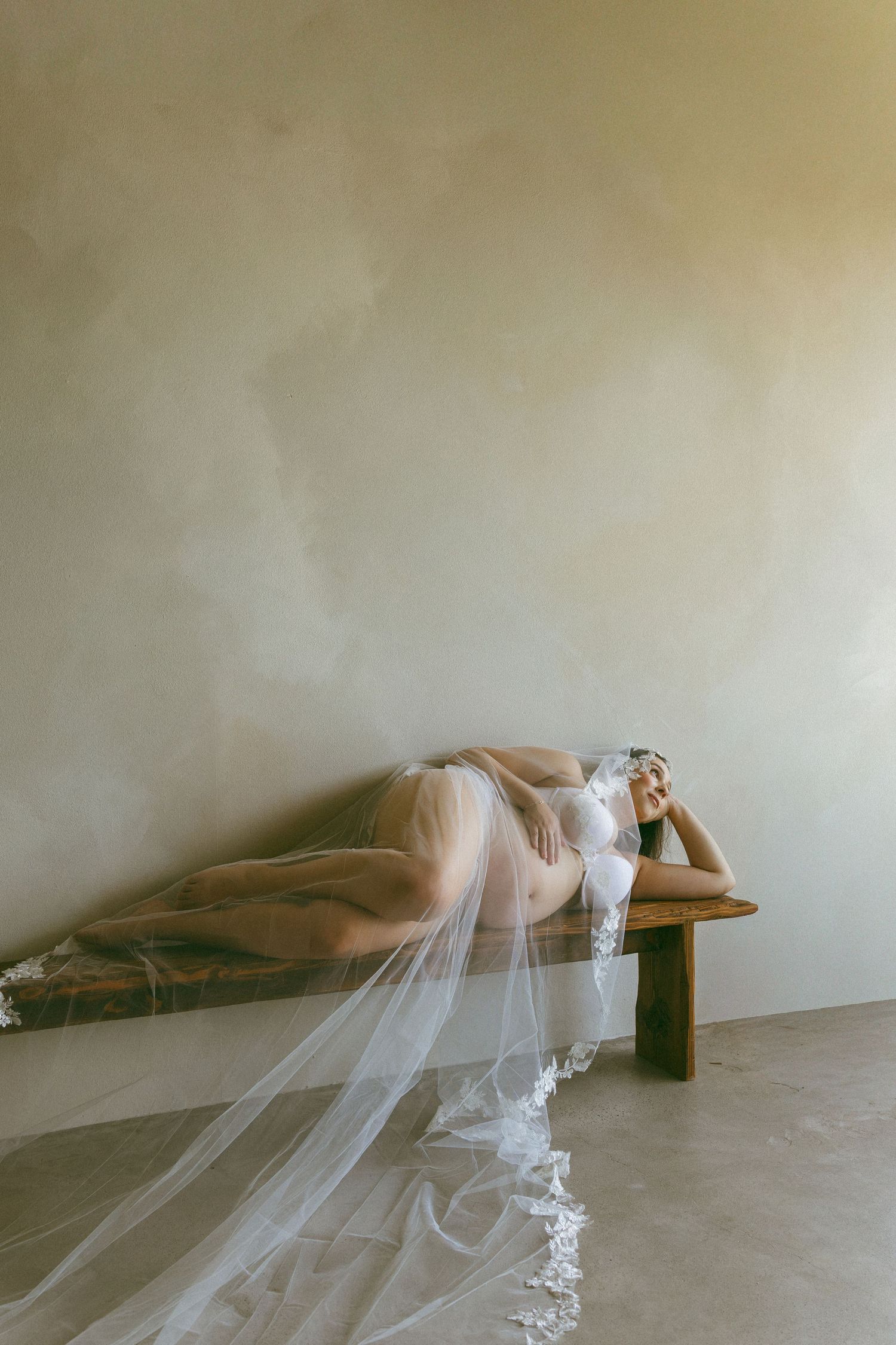 pregnant woman laying on a bench with a wedding veil.