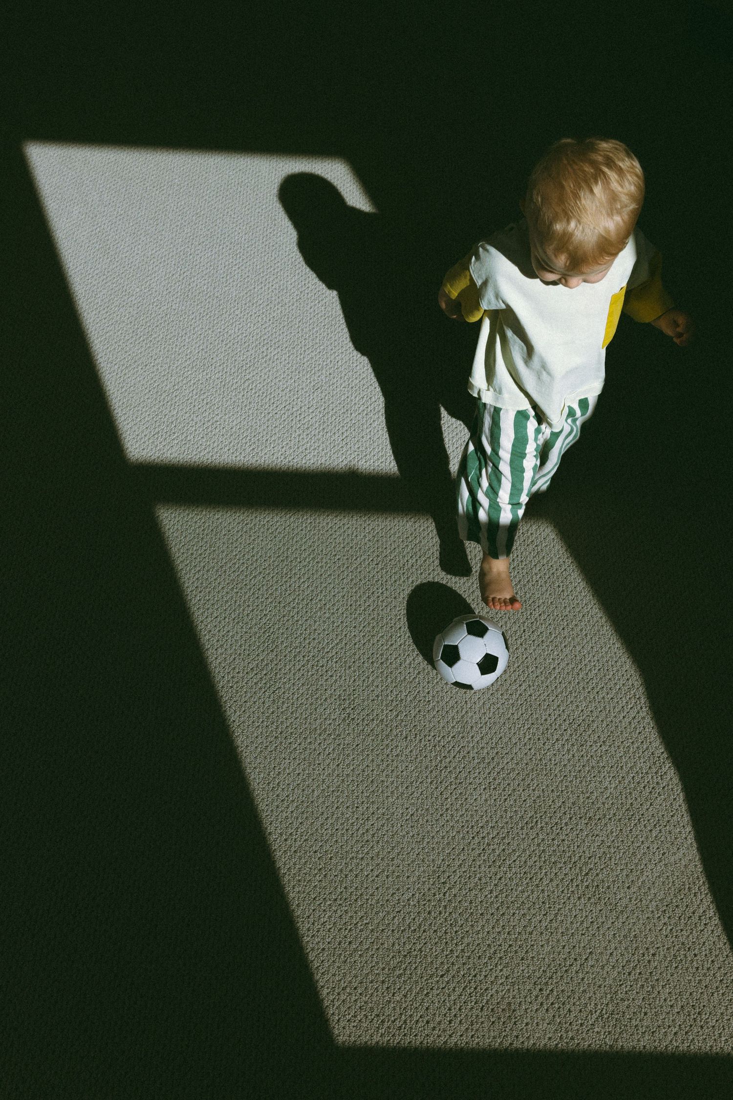 young child playing soccer in the shadows