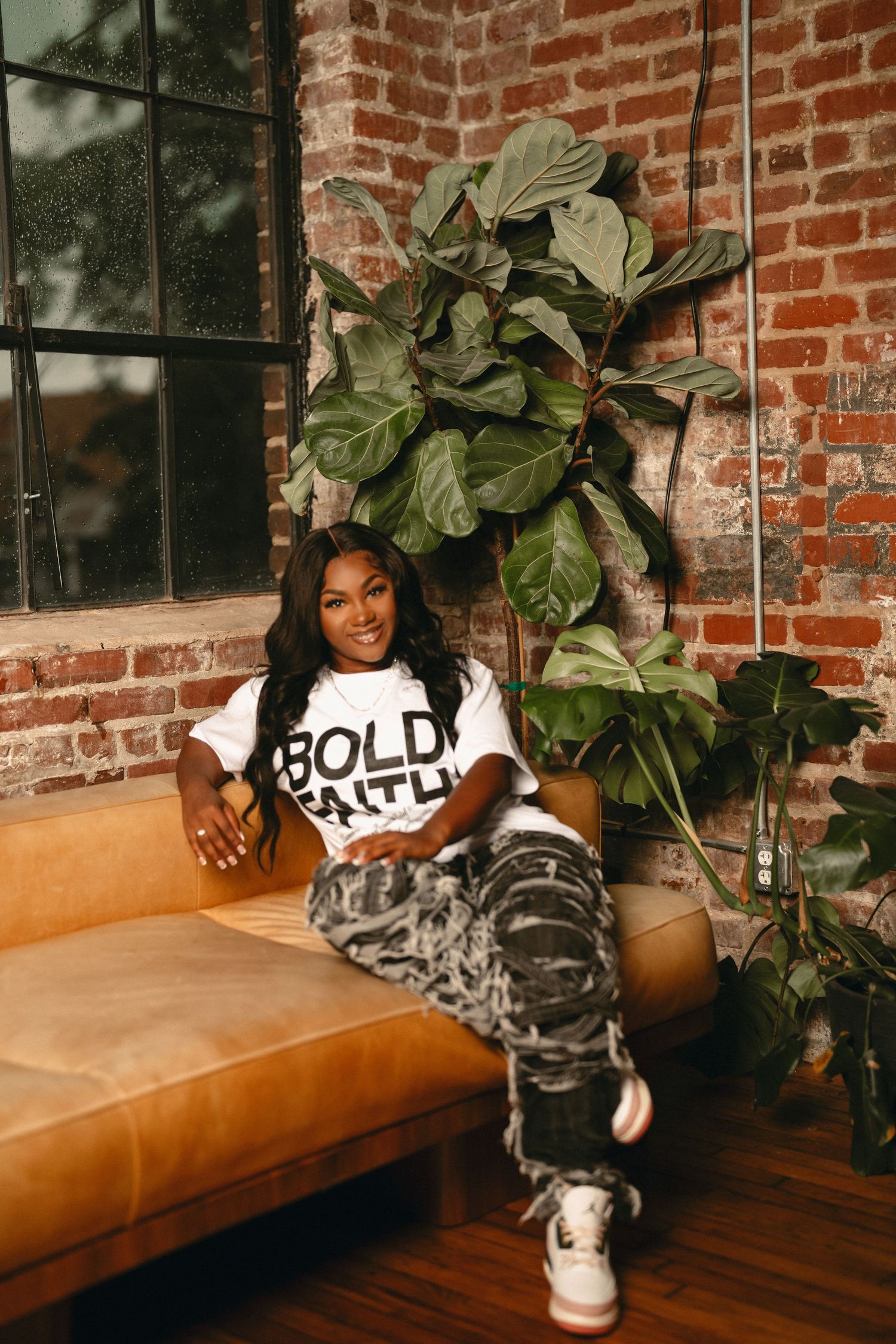 Atlanta branding photography of a woman wearing a Bold Faith graphic T-shirt seated beside indoor plants.