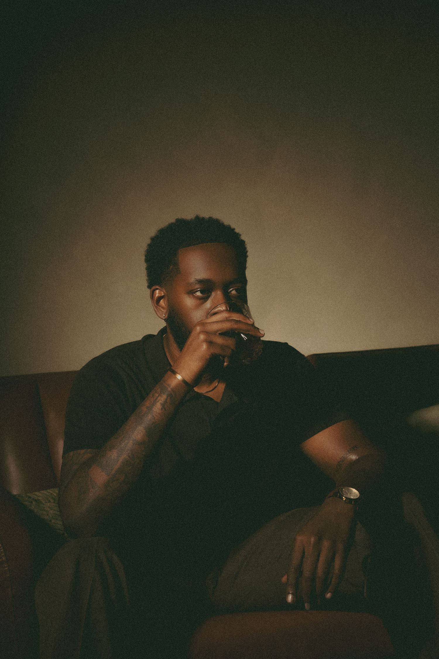 Atlanta portrait photography of a man seated on a leather sofa in moody, low-light surroundings.