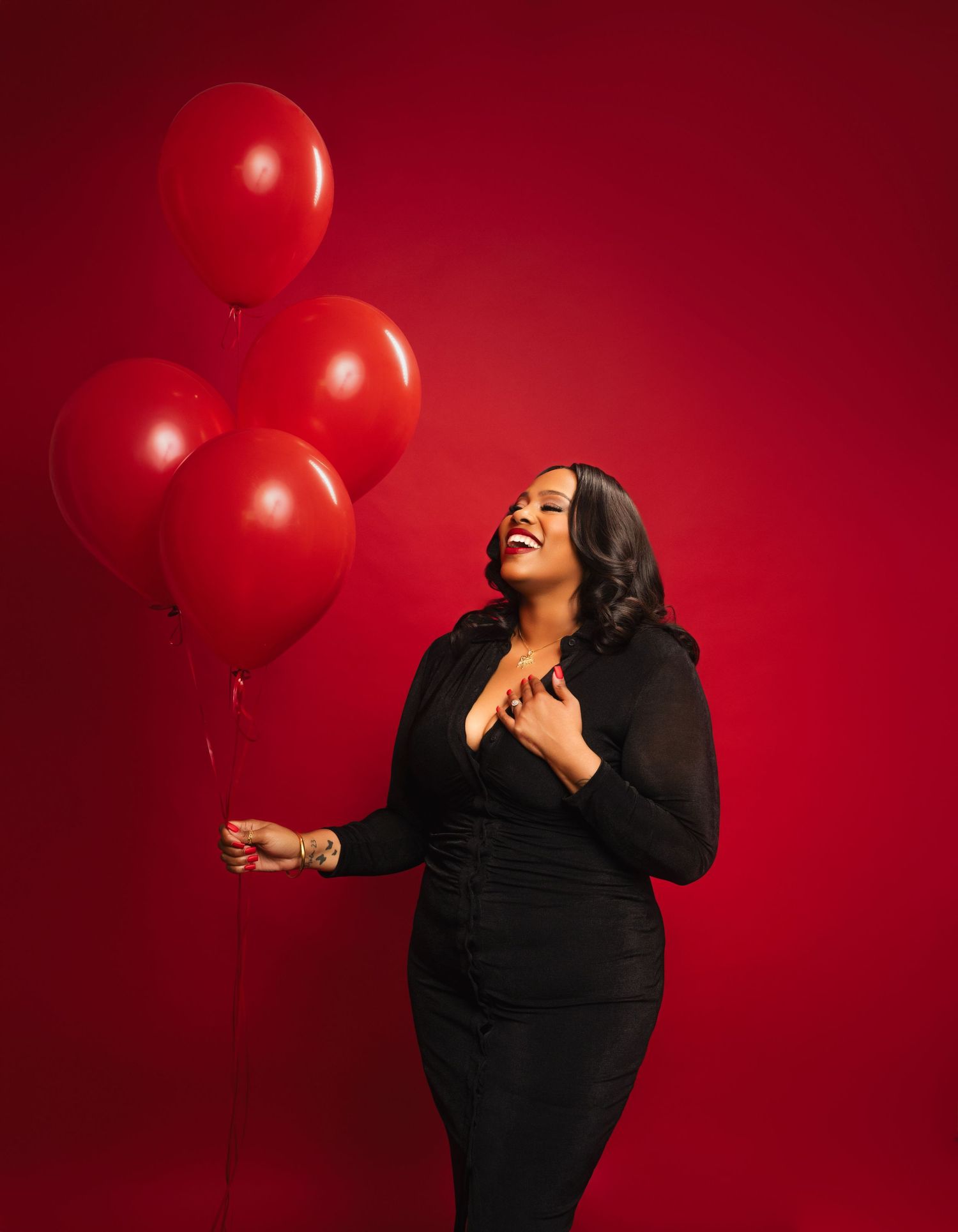 Atlanta in-studio portrait photography of a woman in a black dress holding red balloons against a vibrant red studio backdrop.