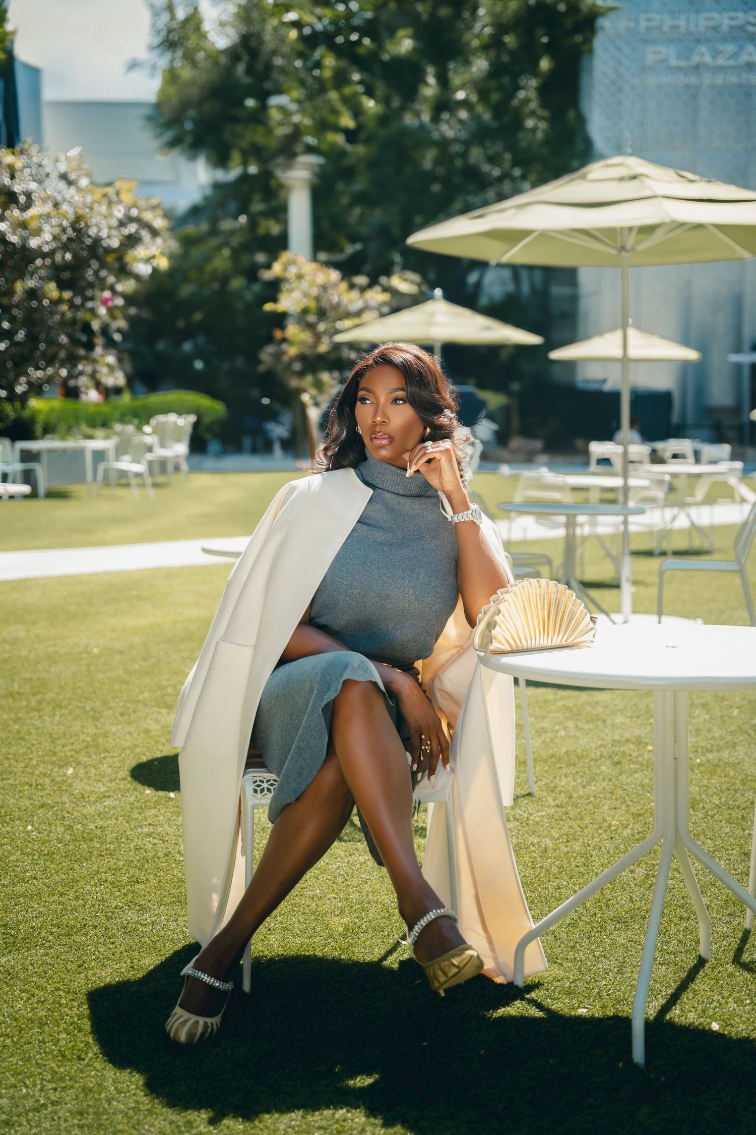 Atlanta lifestyle portrait of a woman in a gray dress and white coat seated outdoors at Phipps Plaza.