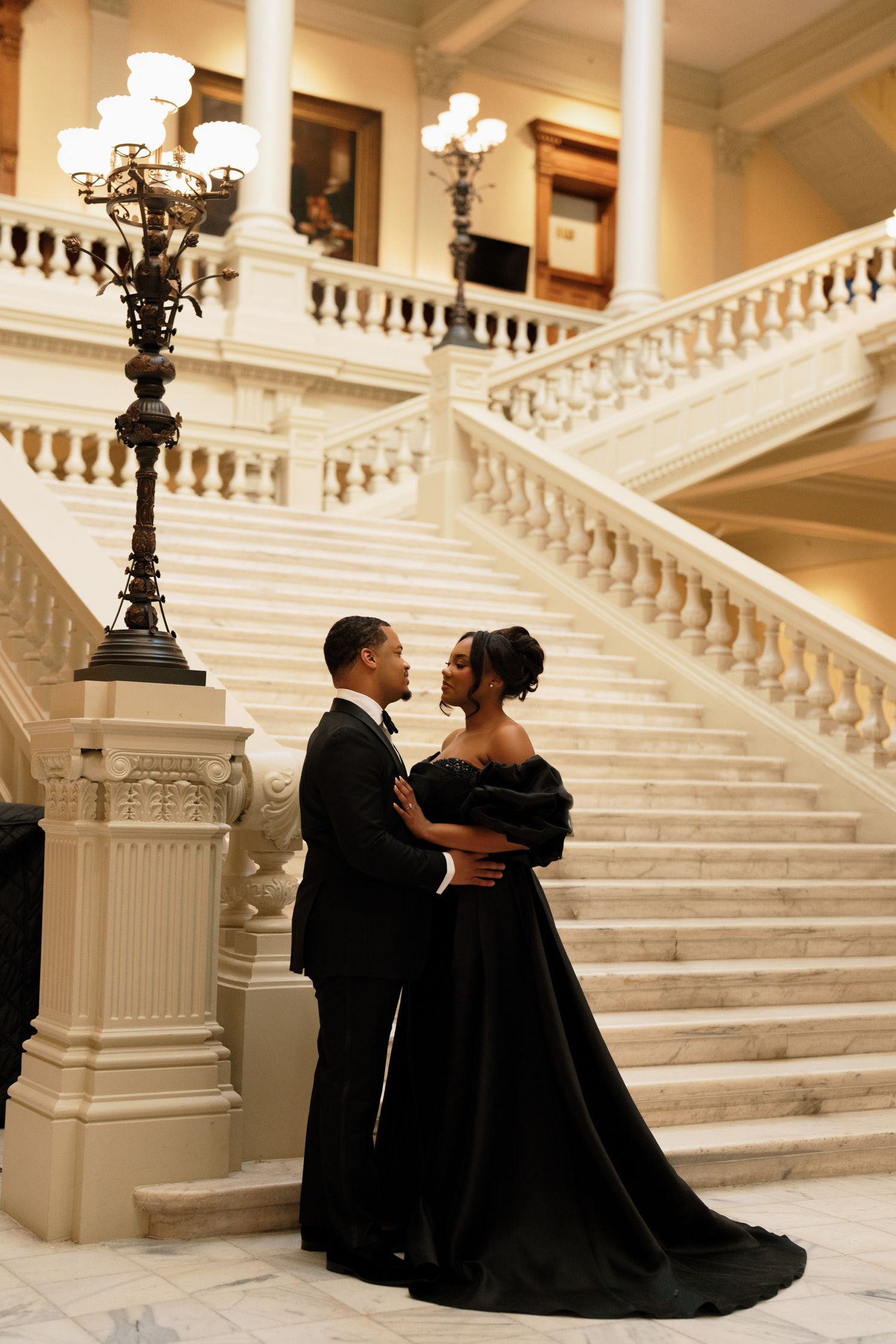 Atlanta couples elopement photography of an elegant couple in black formal attire embracing beside a grand marble staircase.