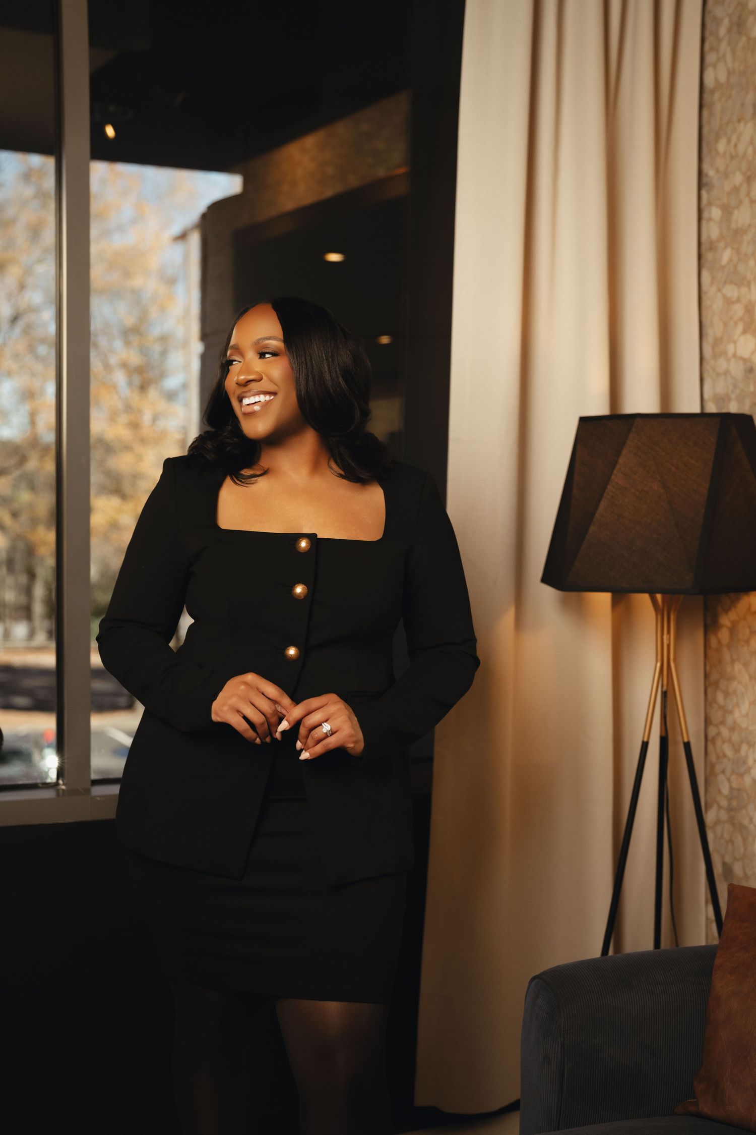 Atlanta business branding portrait of a woman in a black skirt suit smiling beside a sunlit window.