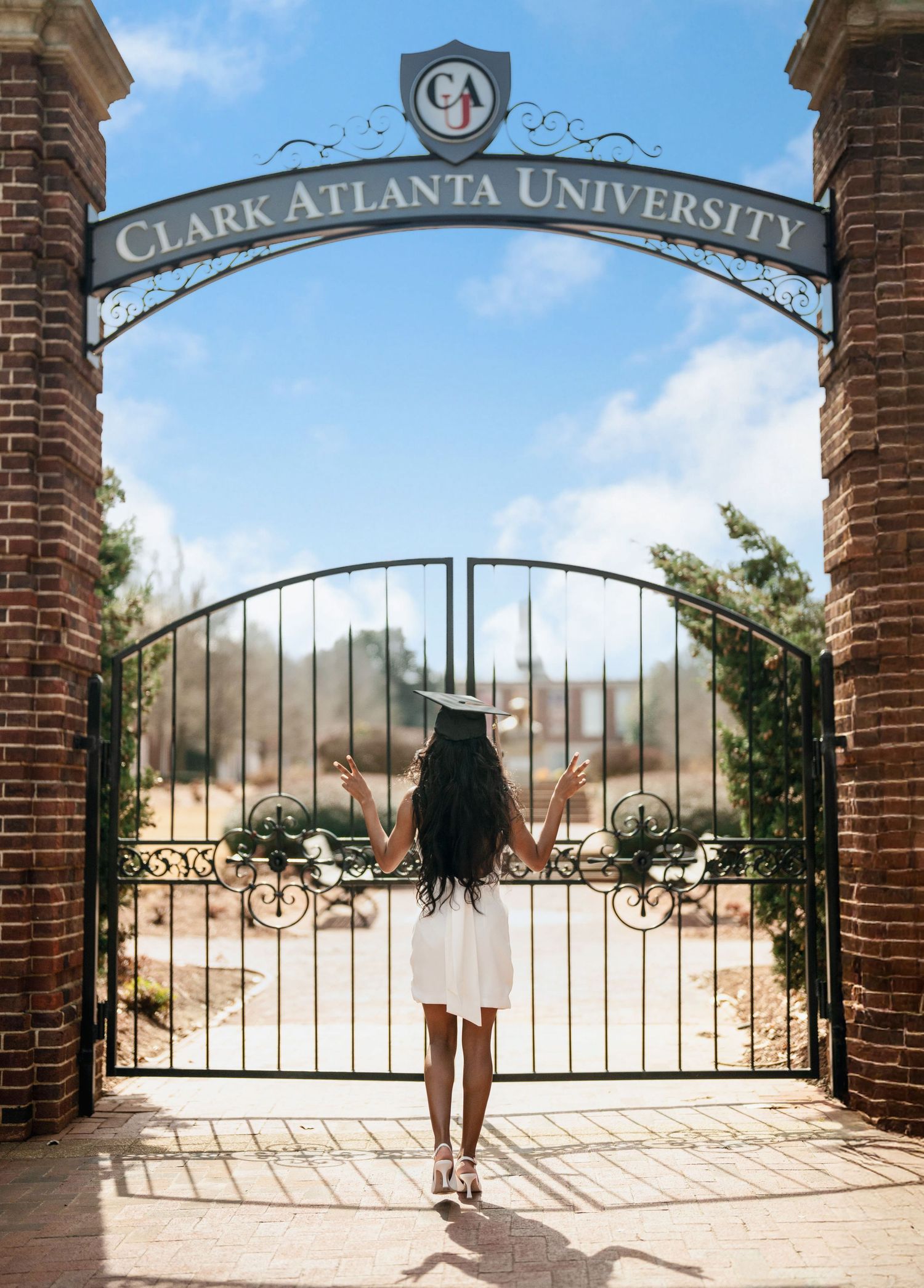 Atlanta graduation photography at Clark Atlanta University featuring a graduate in a white dress and cap at the campus entrance.