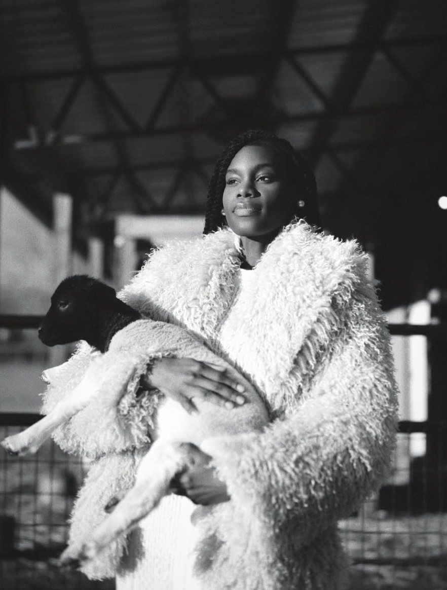 Black-and-white Atlanta branding portrait of a woman in a textured white coat holding a lamb.
