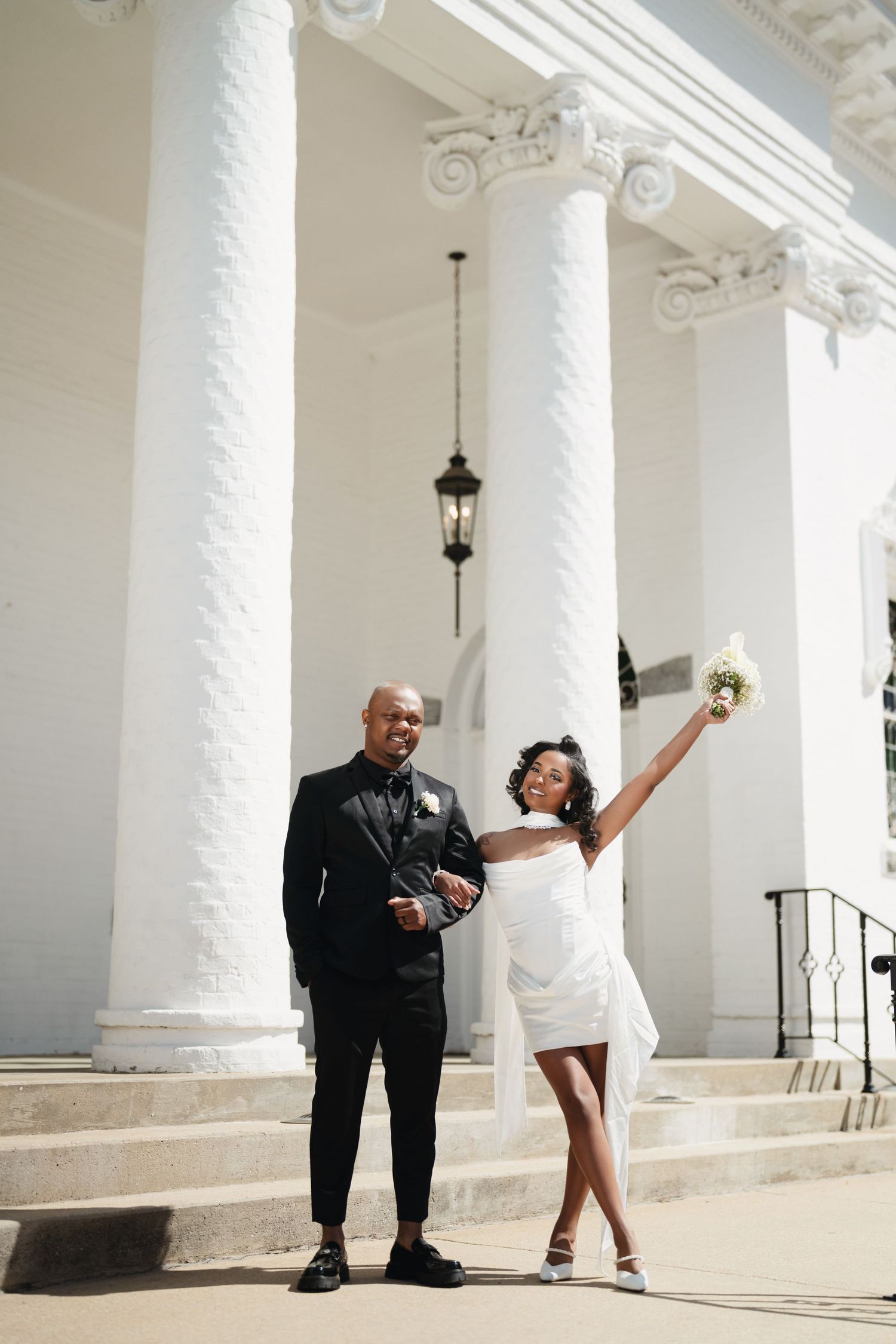 Atlanta wedding photography of a joyful bride raising her bouquet beside the groom at an elegant columned venue.