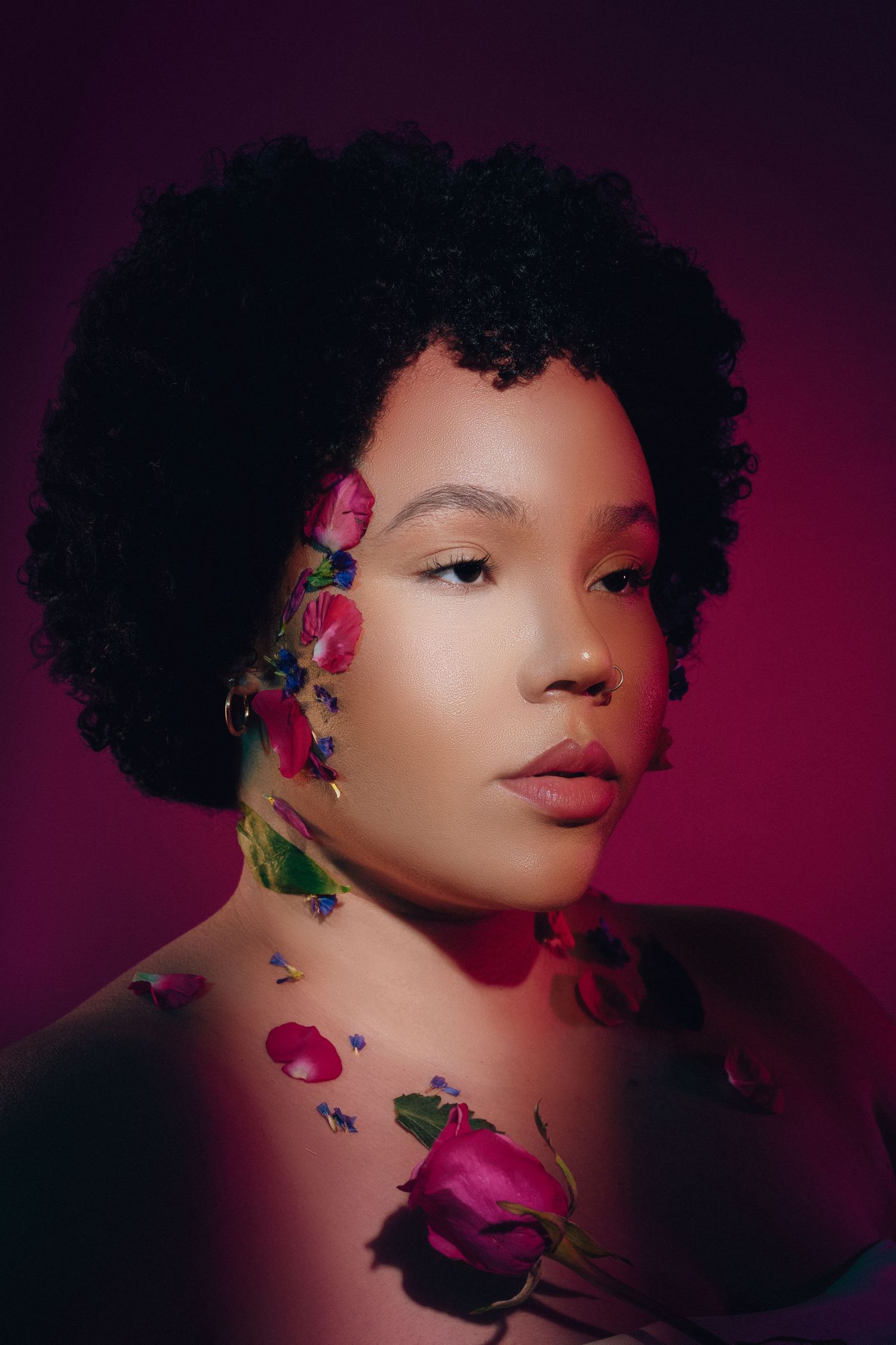 Creative Atlanta in-studio portrait photography of a woman with natural hair and pink roses against a vibrant magenta background.