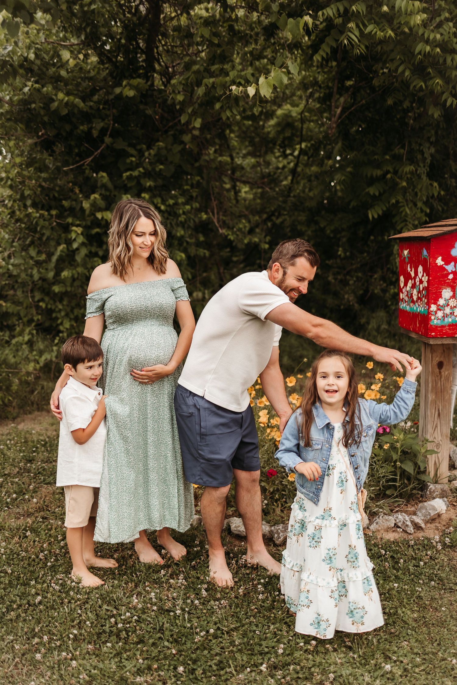 Pregnant woman in green dress with husband and two children posing outdoors near colorful mailbox.