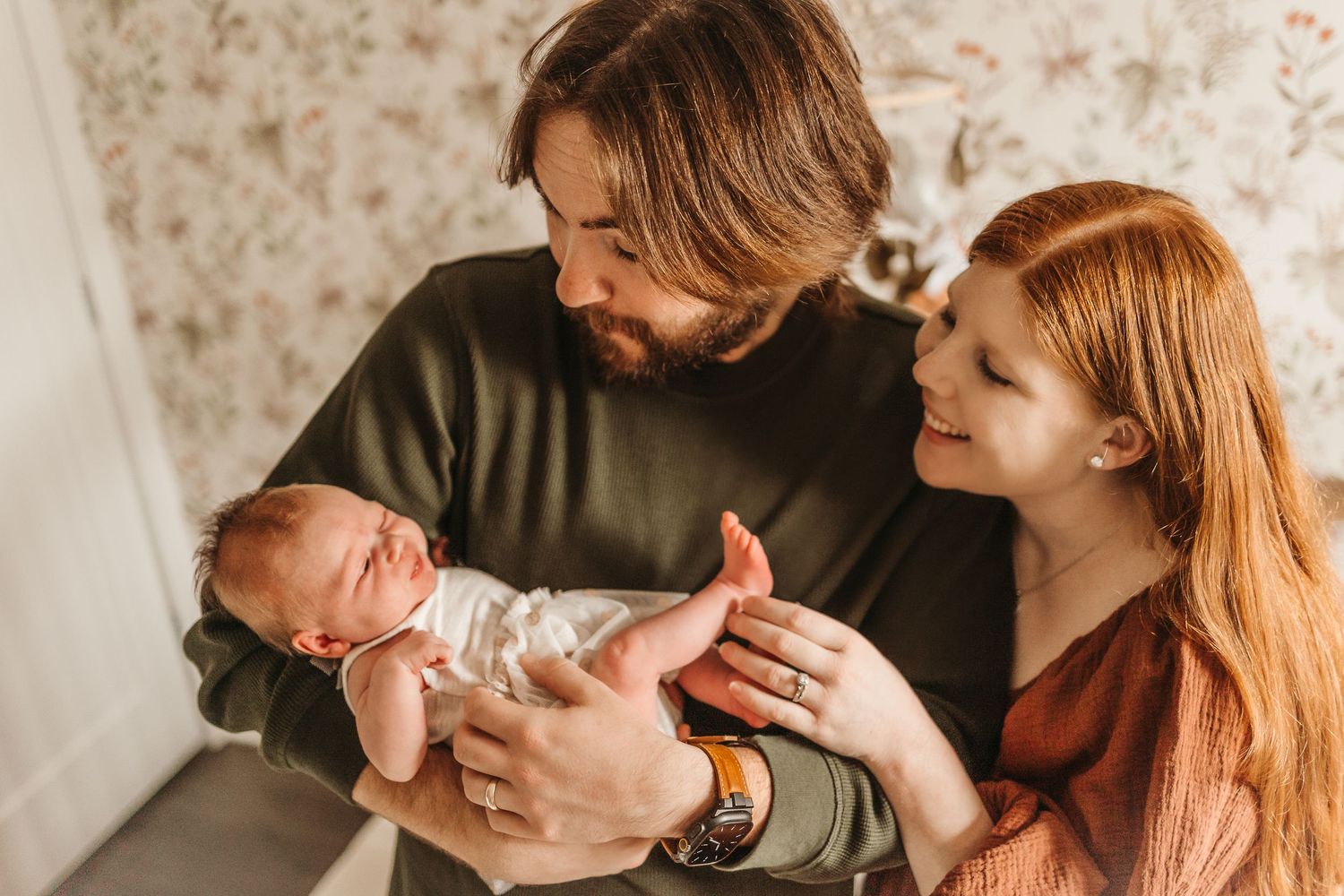 New parents lovingly admire their sleeping newborn baby together in a warm, intimate home setting.