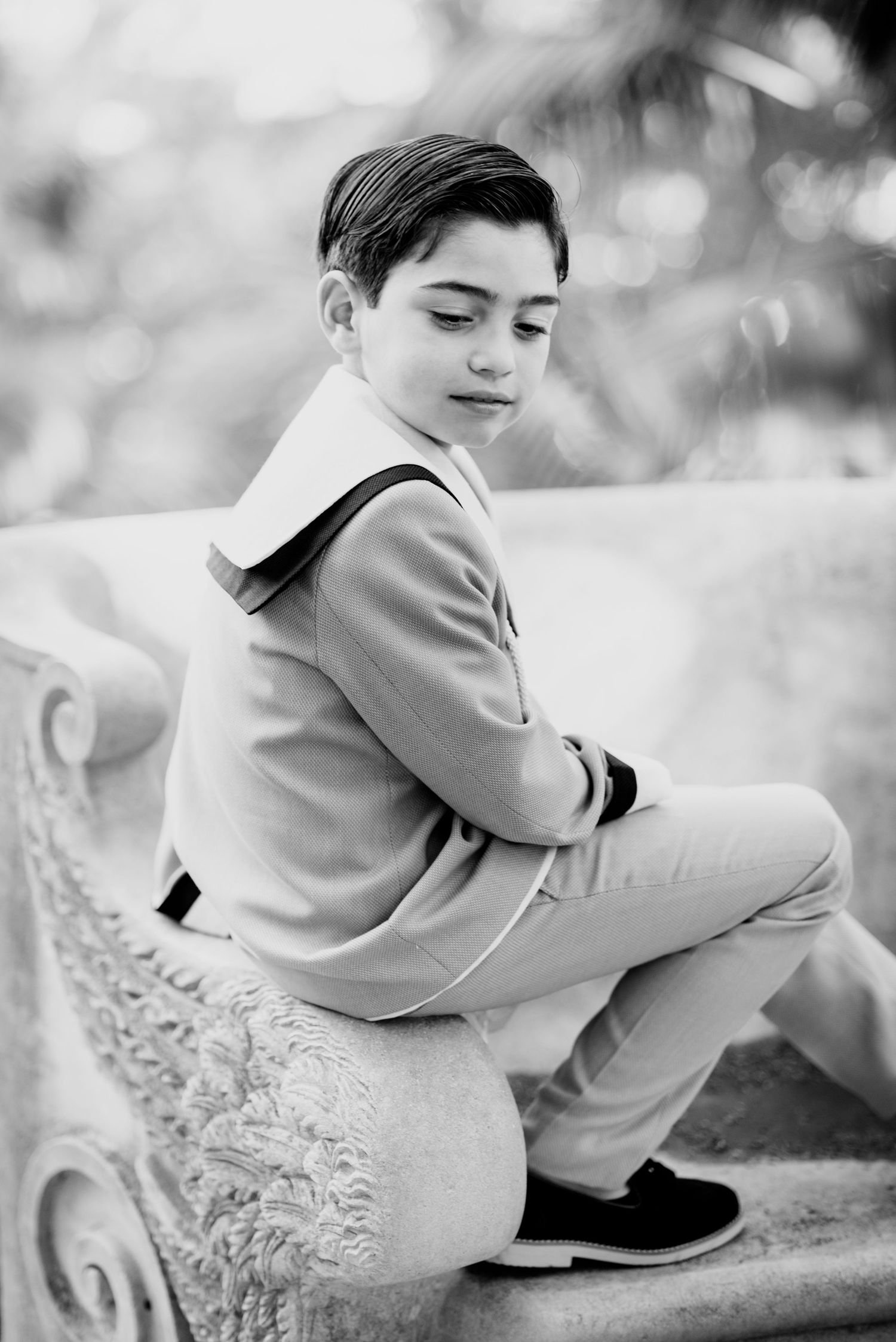 Black and white portrait of boy sitting on ornate bench.