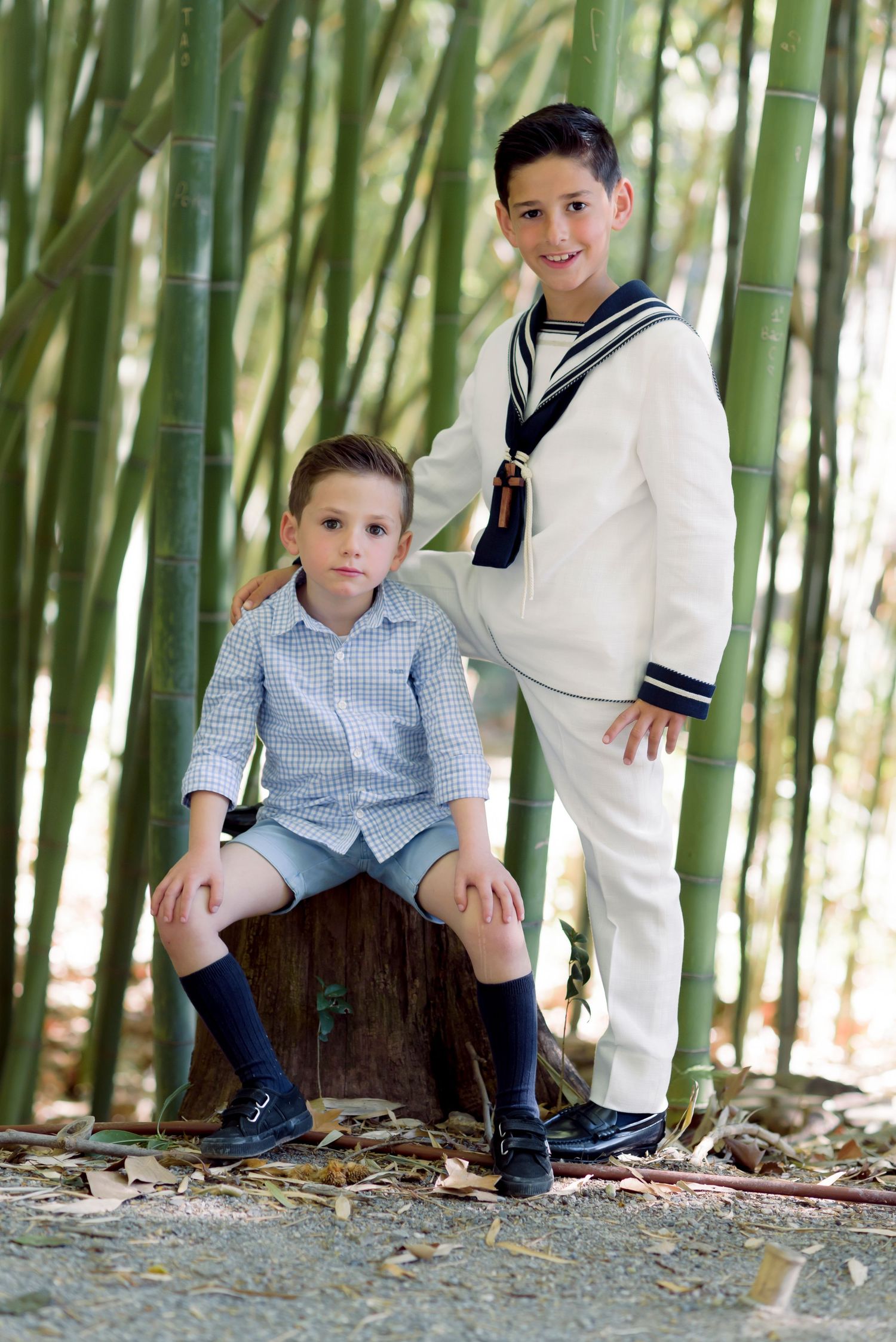 Two boys pose in bamboo grove, one in sailor communion suit, one in blue shirt.