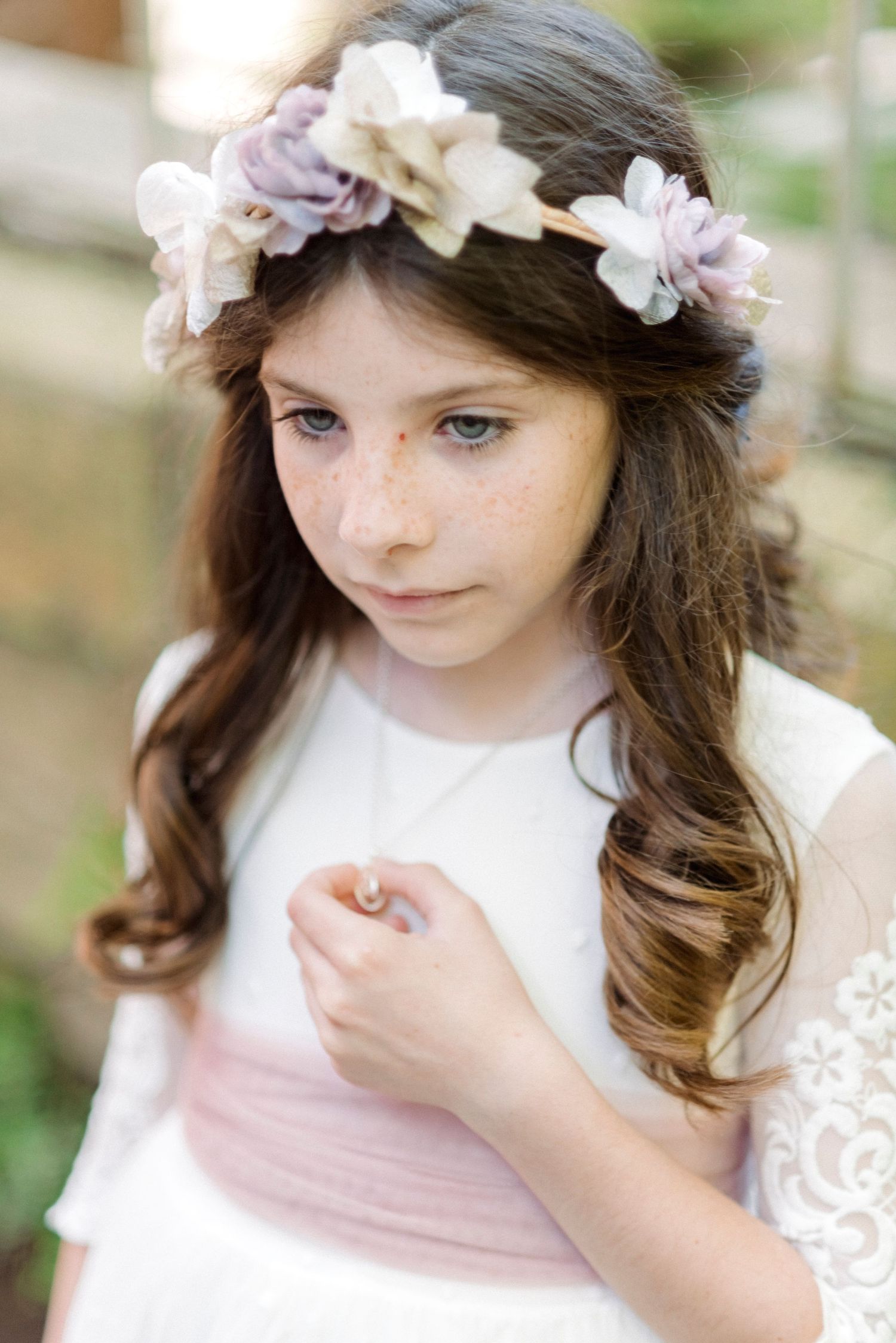 Close-up of girl with freckles wearing purple floral crown and white lace dress with pink sash.