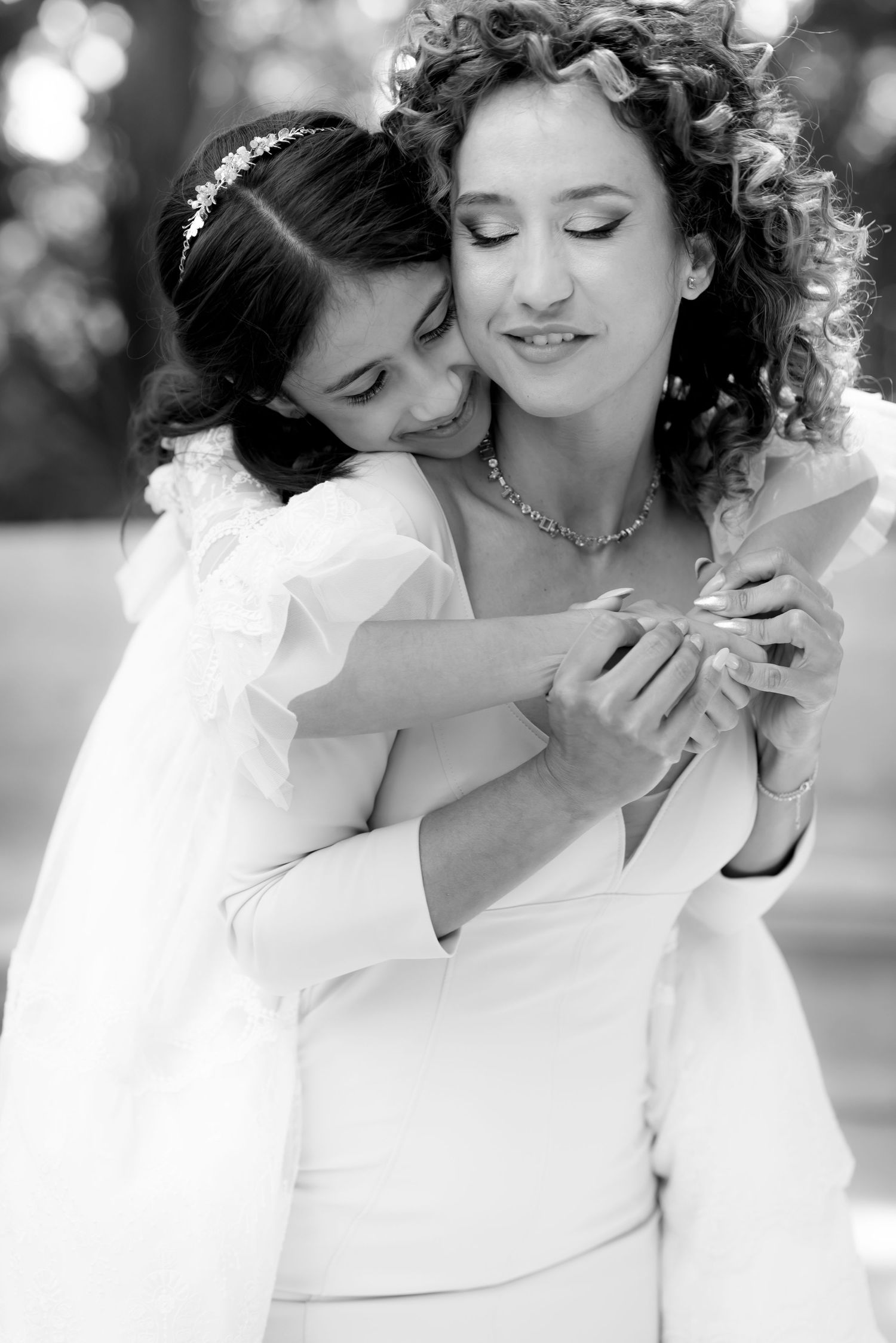 Black and white photo of a bride and flower girl in white dresses sharing a tender embrace.