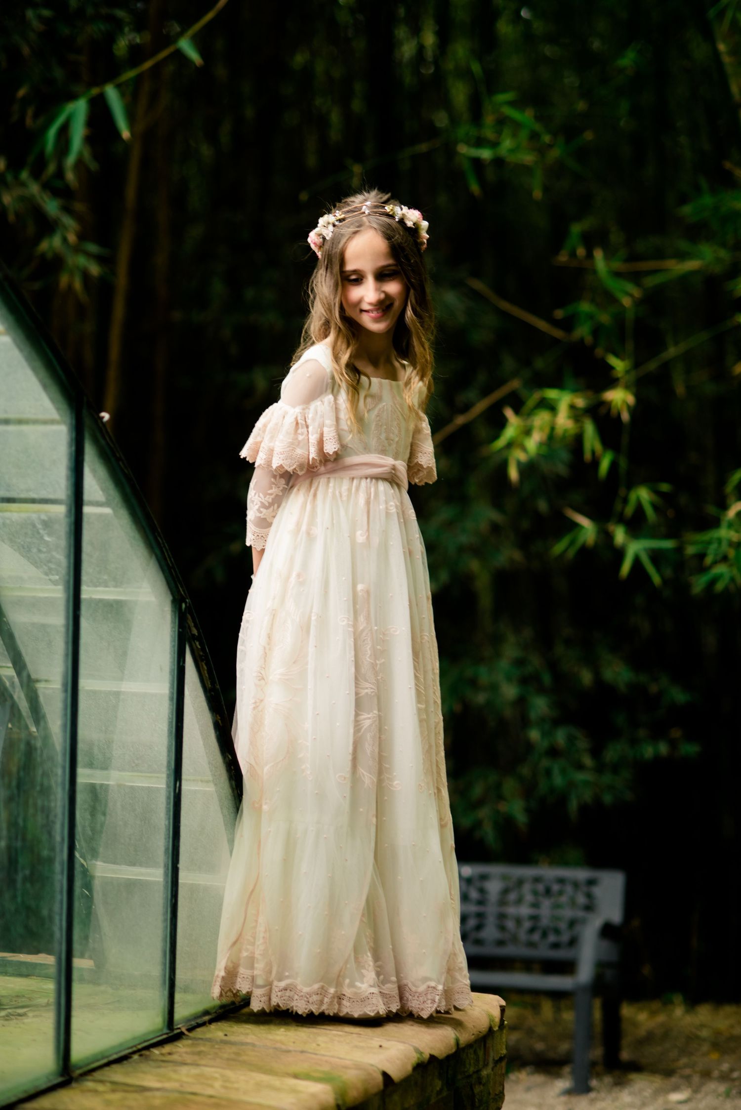 Smiling girl in ivory lace dress with flower crown outdoors.