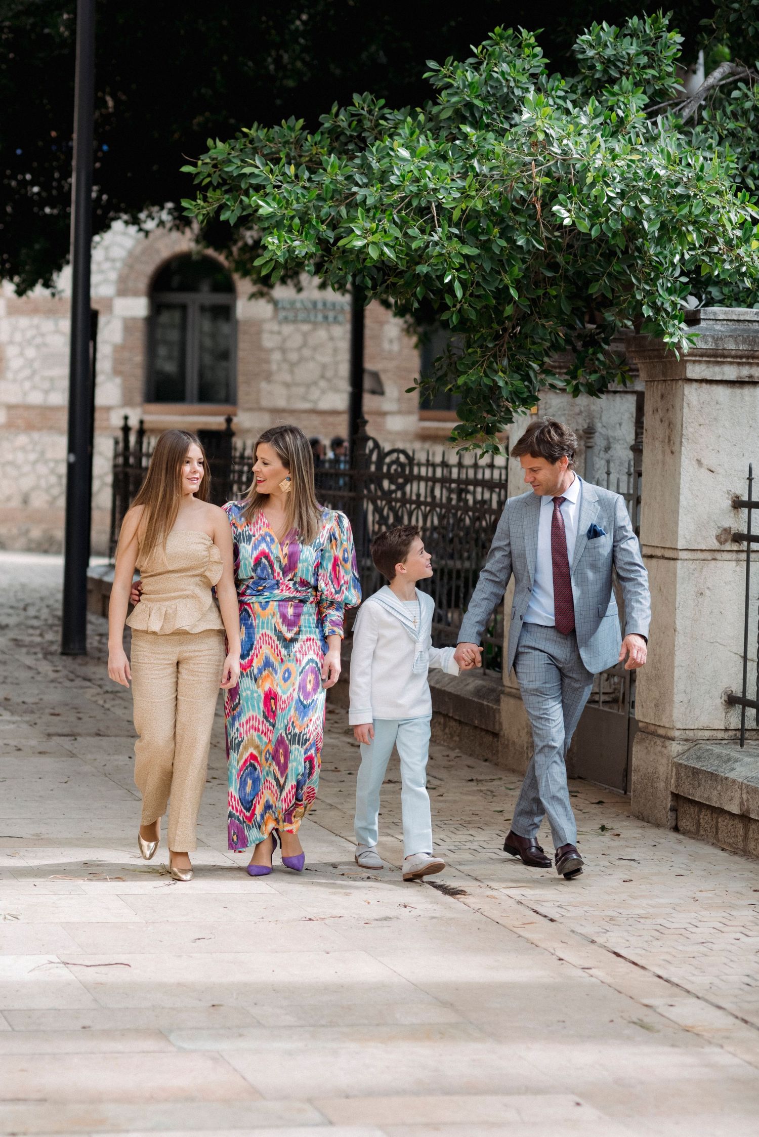 Family of four walks together outdoors, dressed in elegant formal attire for special occasion.