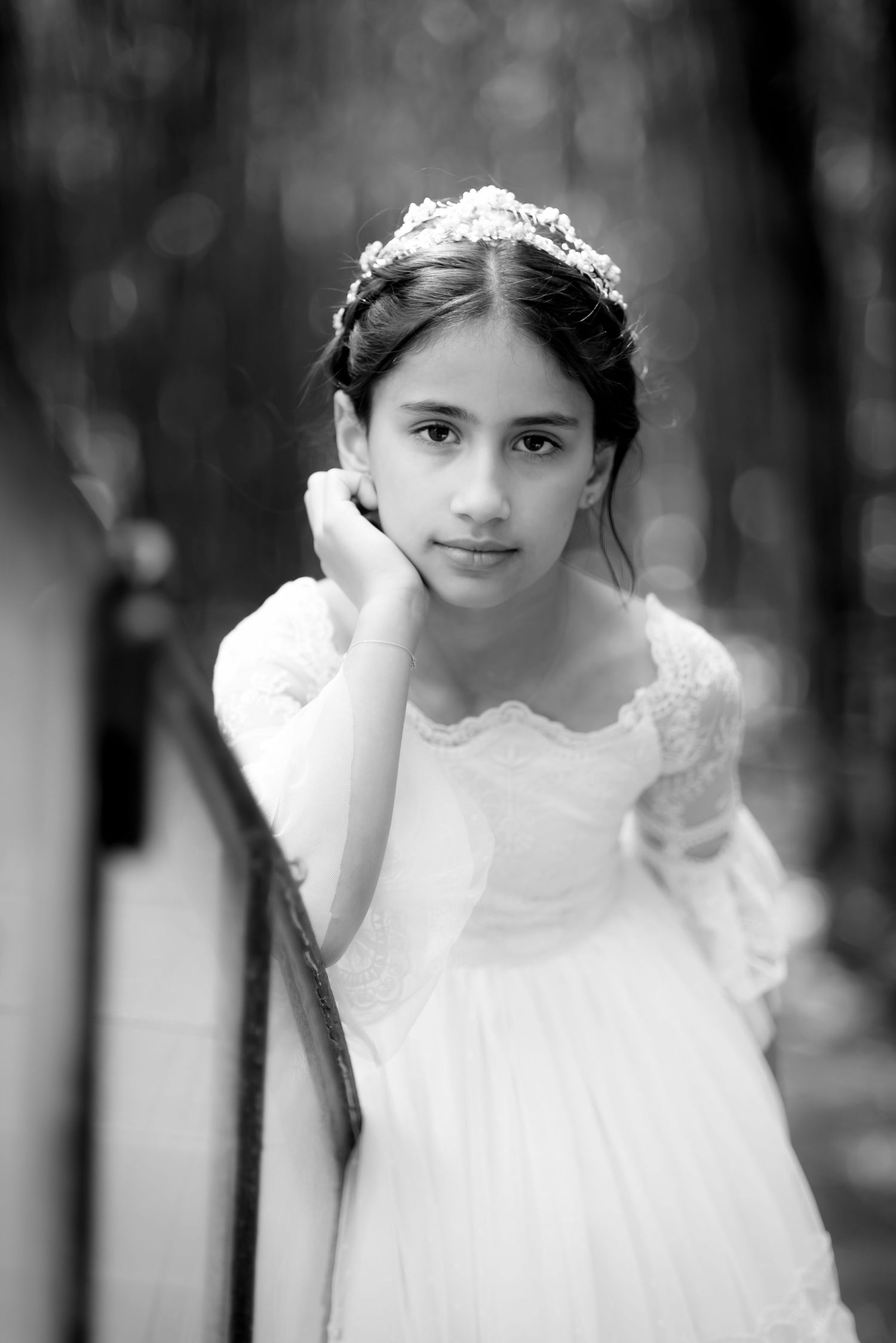 Black and white portrait of girl in white communion dress and crystal tiara outdoors.