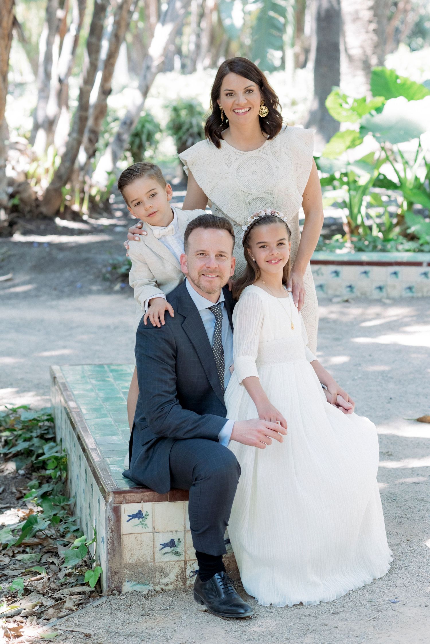 A happy family of four poses together in a lush garden, dressed in elegant formal attire.