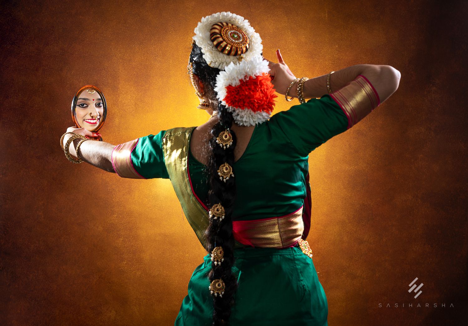 Dancer in a green traditional outfit with flowers posing against a warm, textured background.