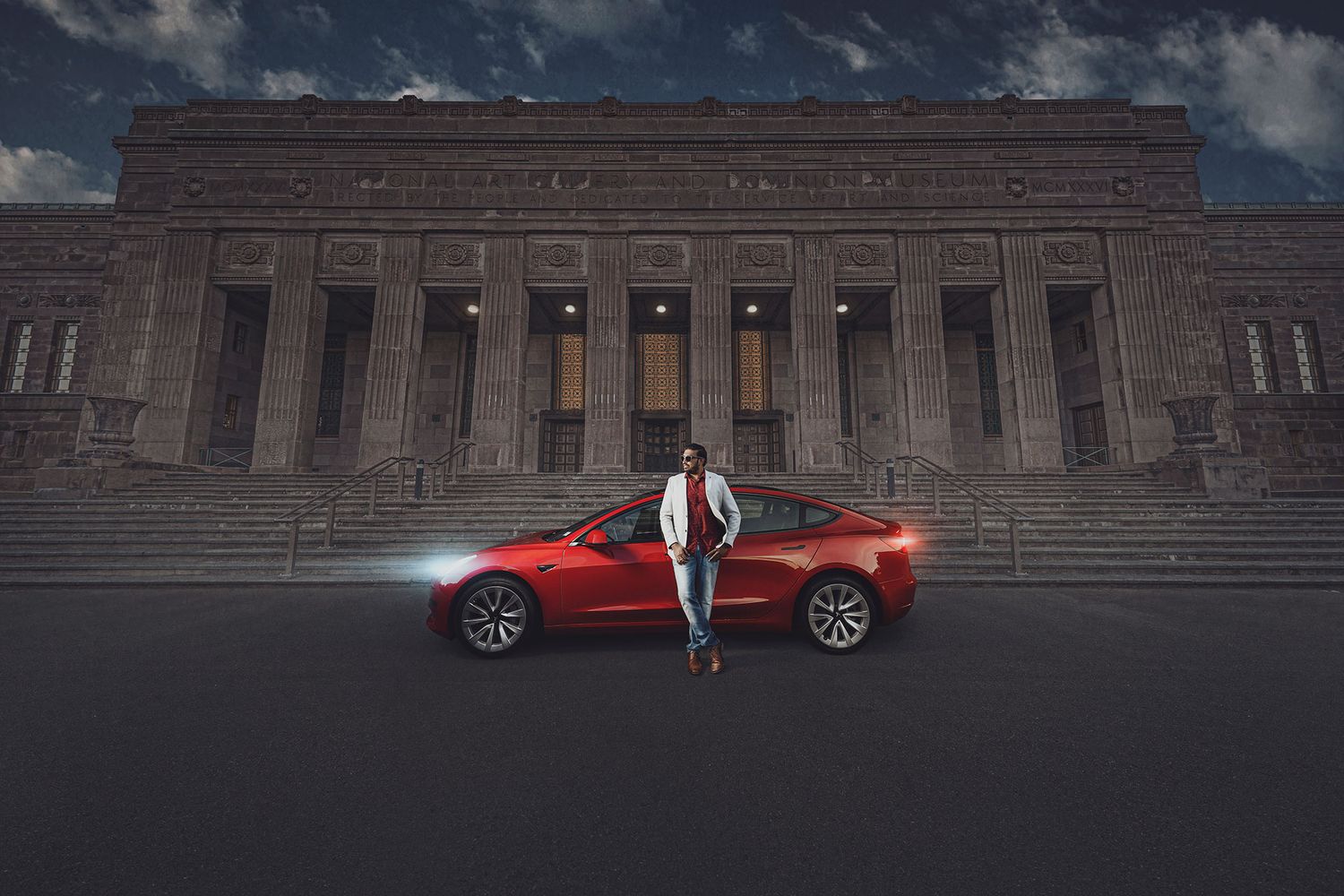 Person in a white jacket and blue jeans standing next to a red car in front of a historic building with columns and stairs.