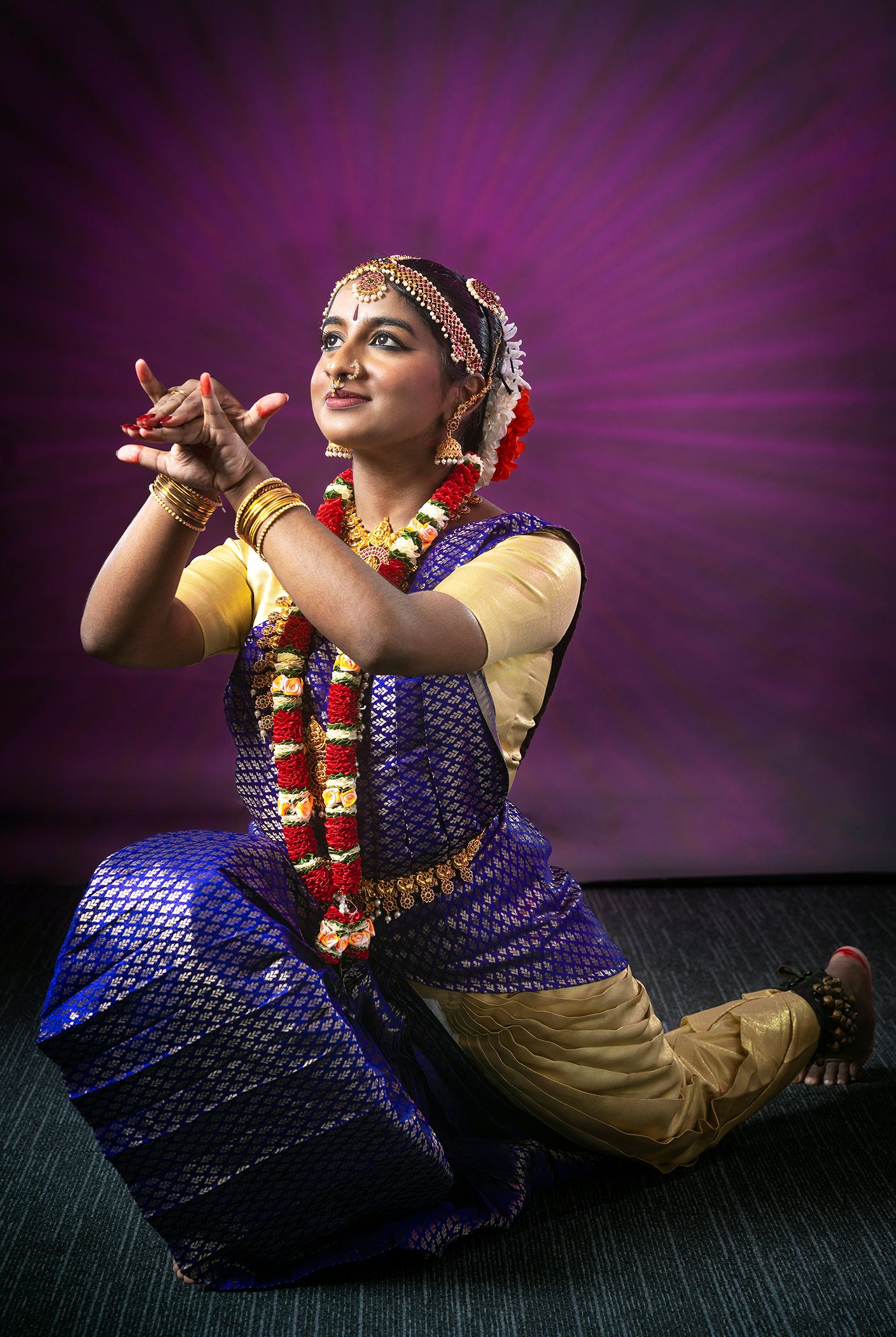 Dancer in traditional Indian costume performing classical dance against purple backdrop.