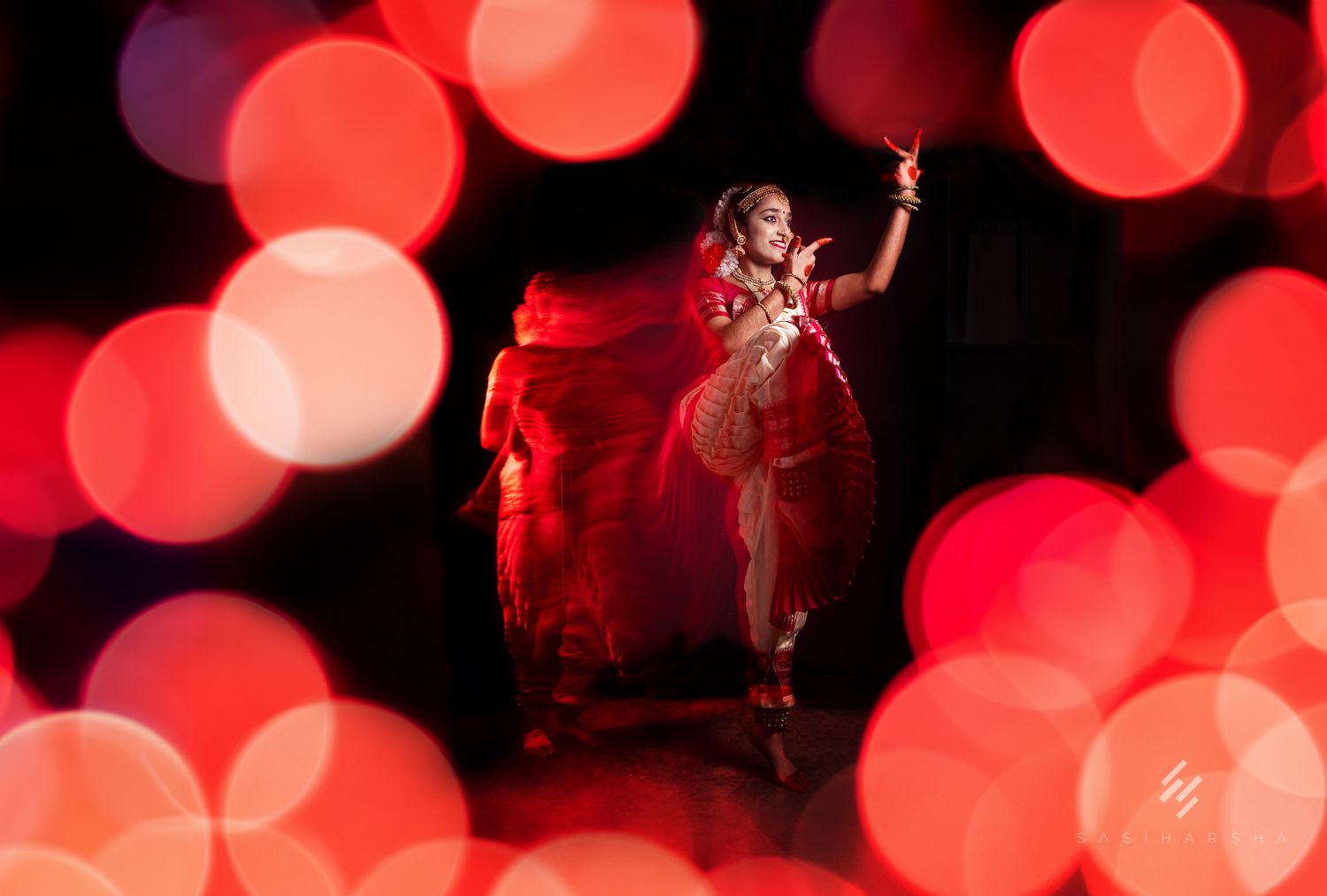 Dancer in traditional attire posing amid vibrant red and soft-focus lights, creating a festive atmosphere.