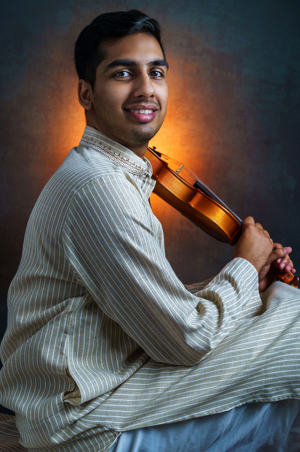 Musician in white striped shirt posing with violin against dark background.