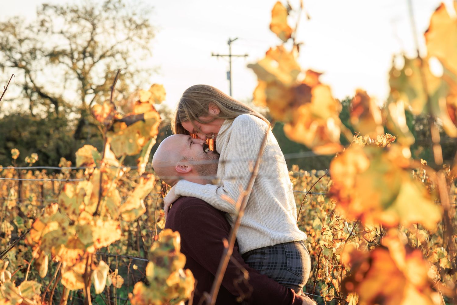 A couple shares a loving moment outdoors, surrounded by golden autumn foliage and a serene, rustic backdrop.