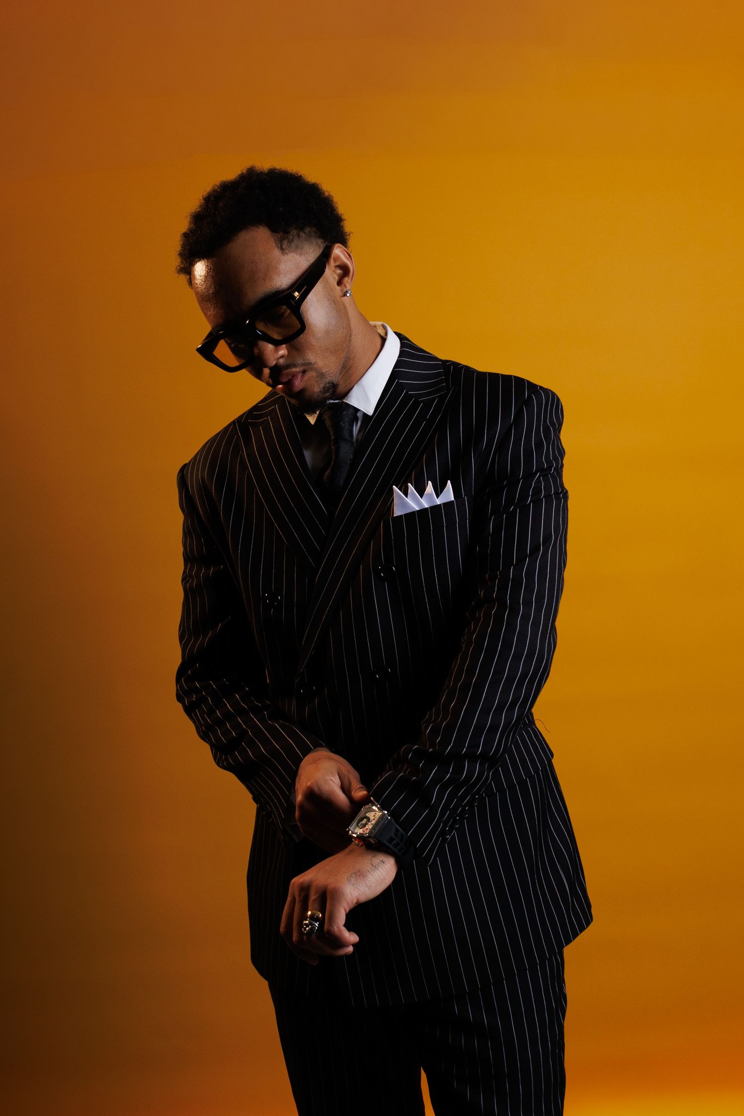 Person in pinstripe suit and sunglasses poses against orange backdrop in dynamic sequence of dance-like movements.