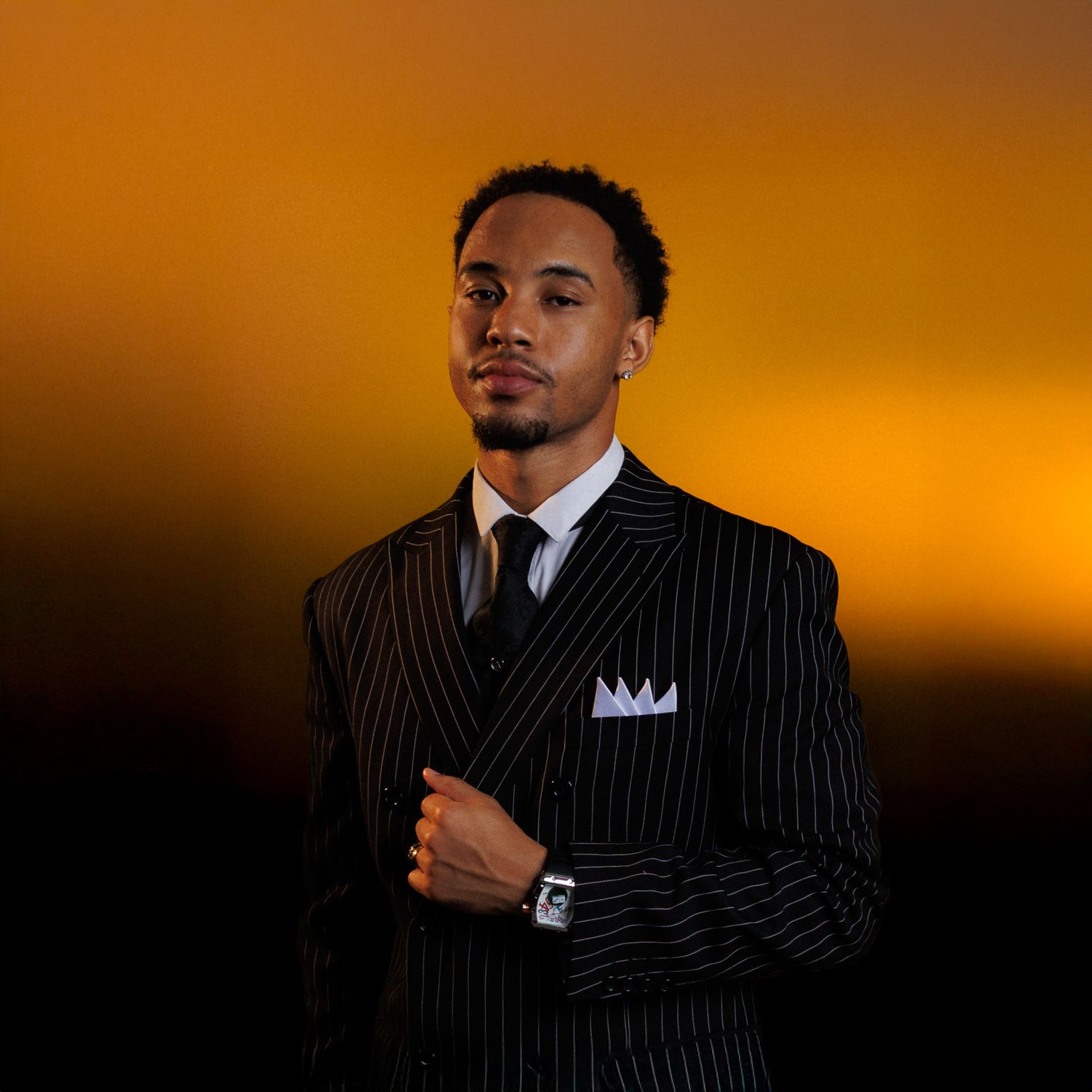 A person in a pinstriped suit poses against an orange sunset backdrop in a series of dramatic portraits.