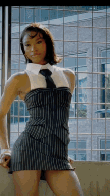 Woman in striped pinstripe mini dress with white collar and black tie posing confidently outdoors.