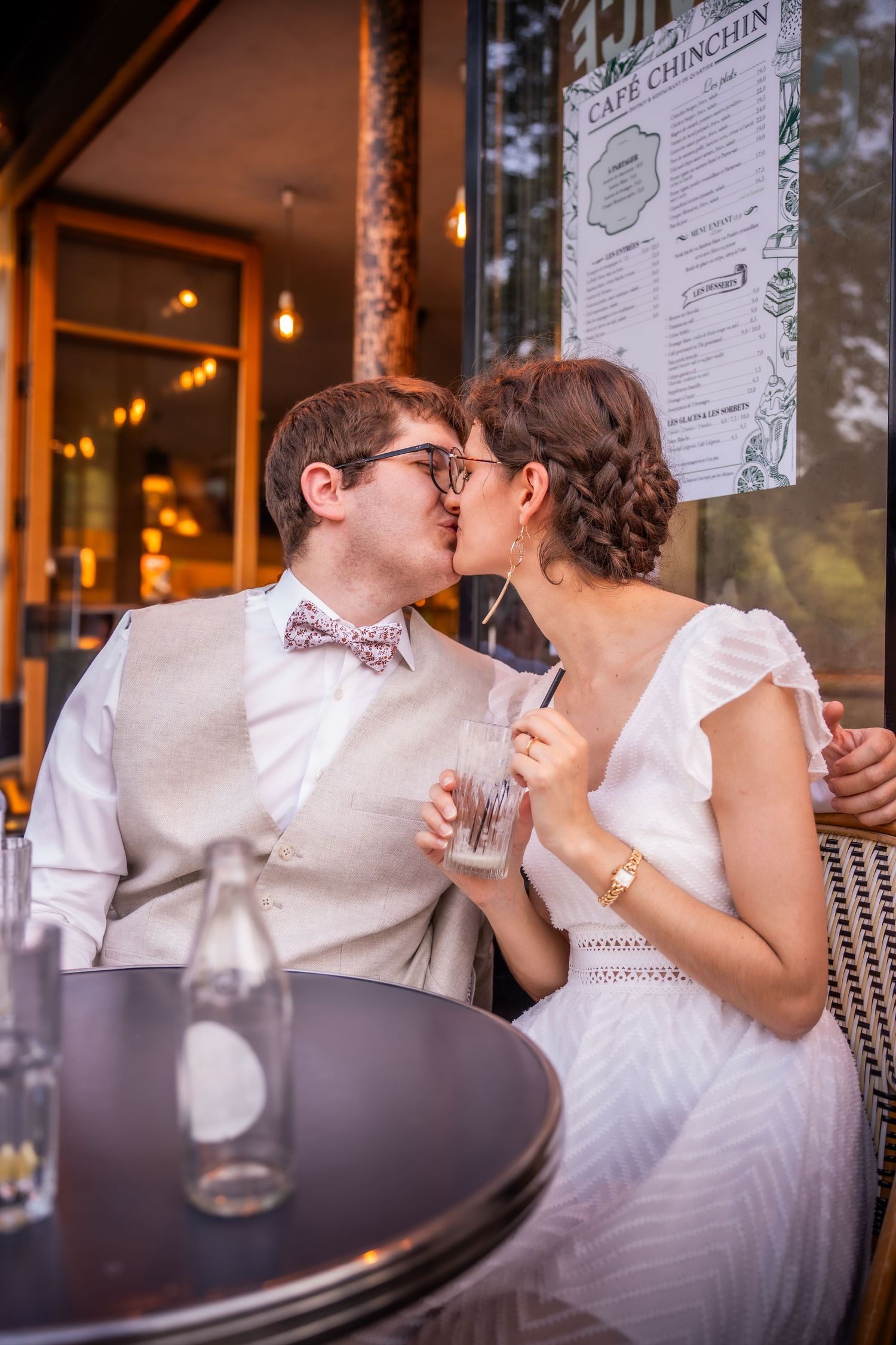 Newlywed couple sharing a kiss at Cafe Chinchin, groom in bow tie and vest, bride in white dress holding drinks.