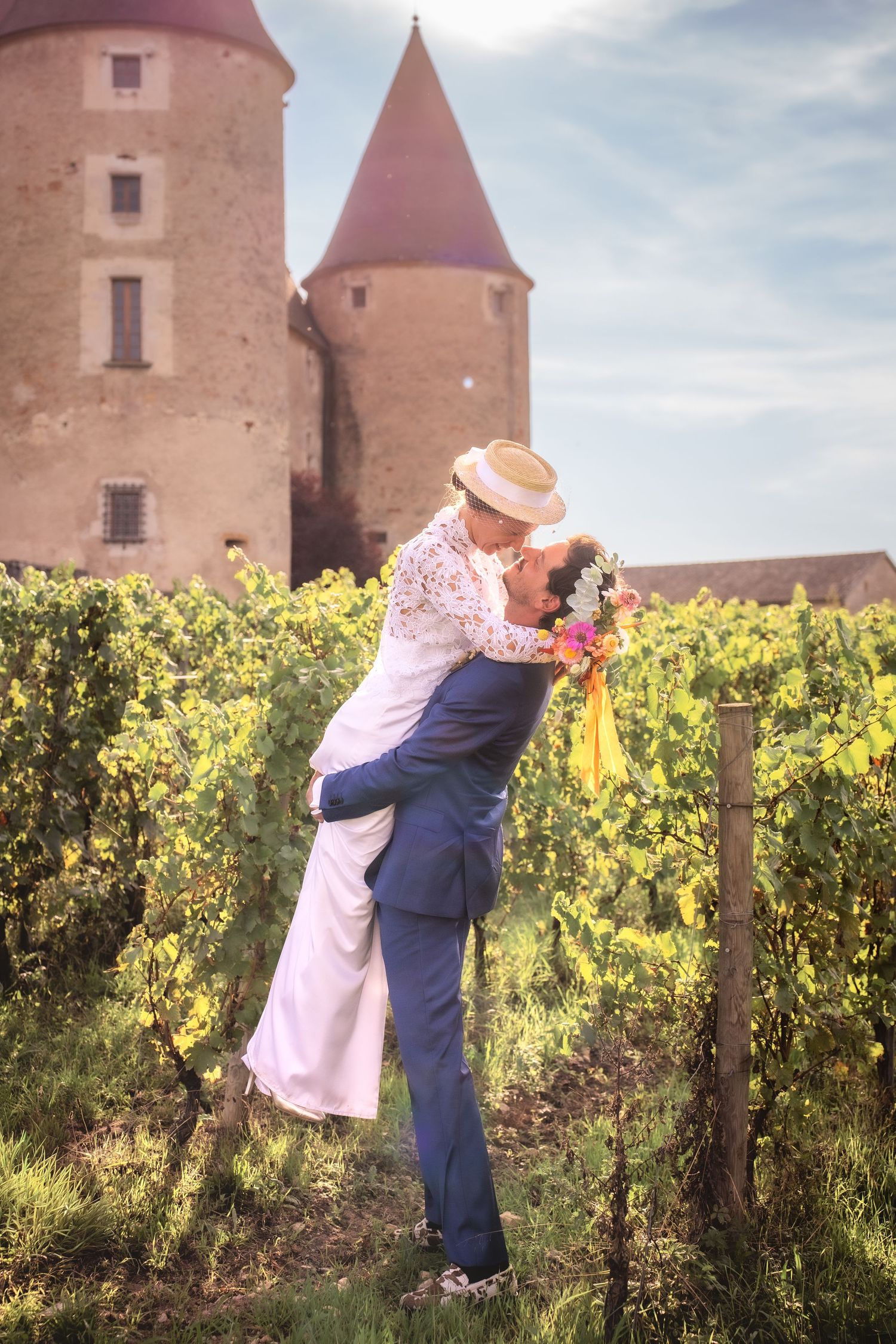 Couple sharing a romantic kiss in a vineyard with a historic French castle in the background on their wedding day.