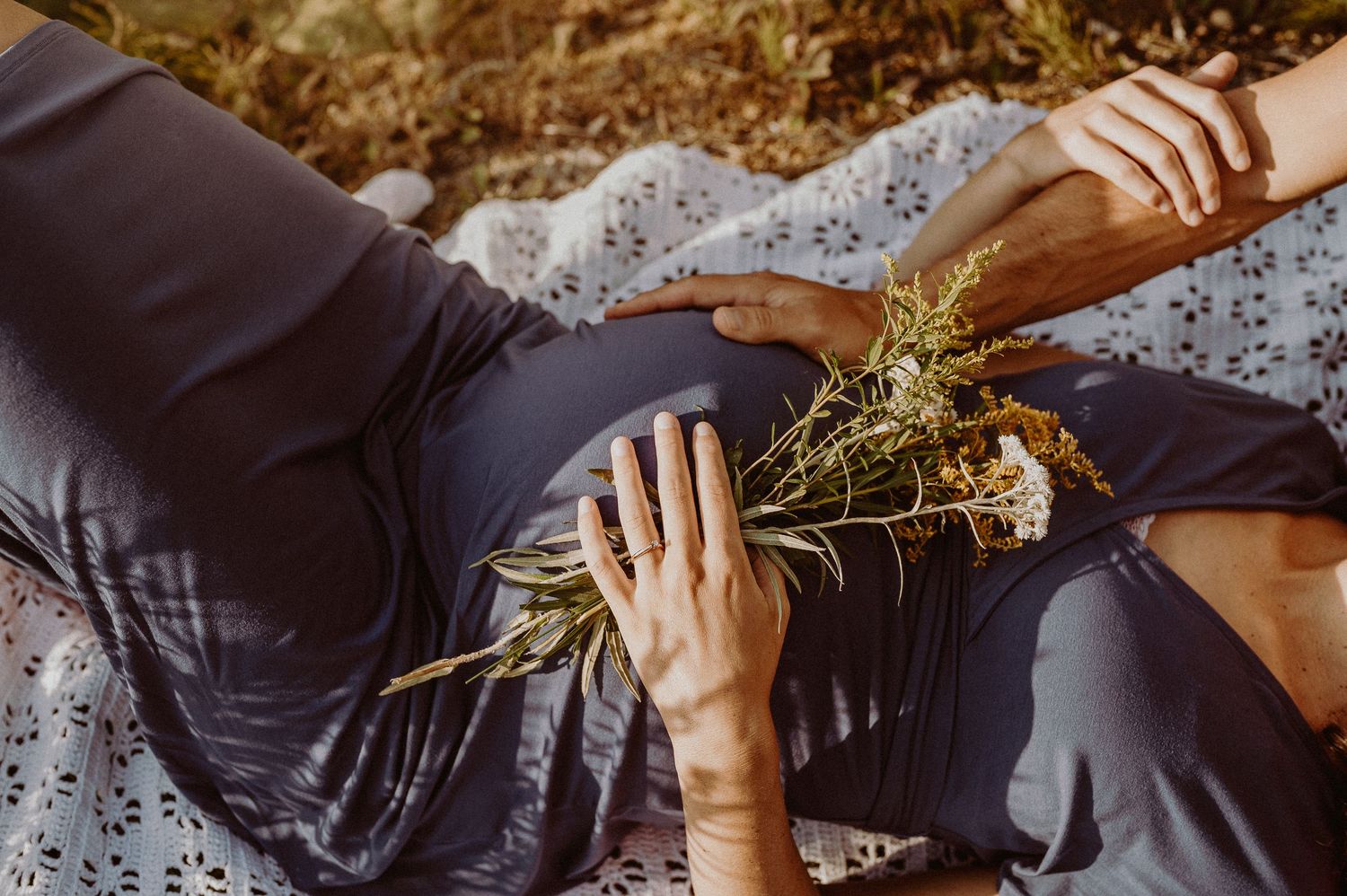 Des mains tiennent des fleurs sauvages en reposant sur une couverture en plein air.