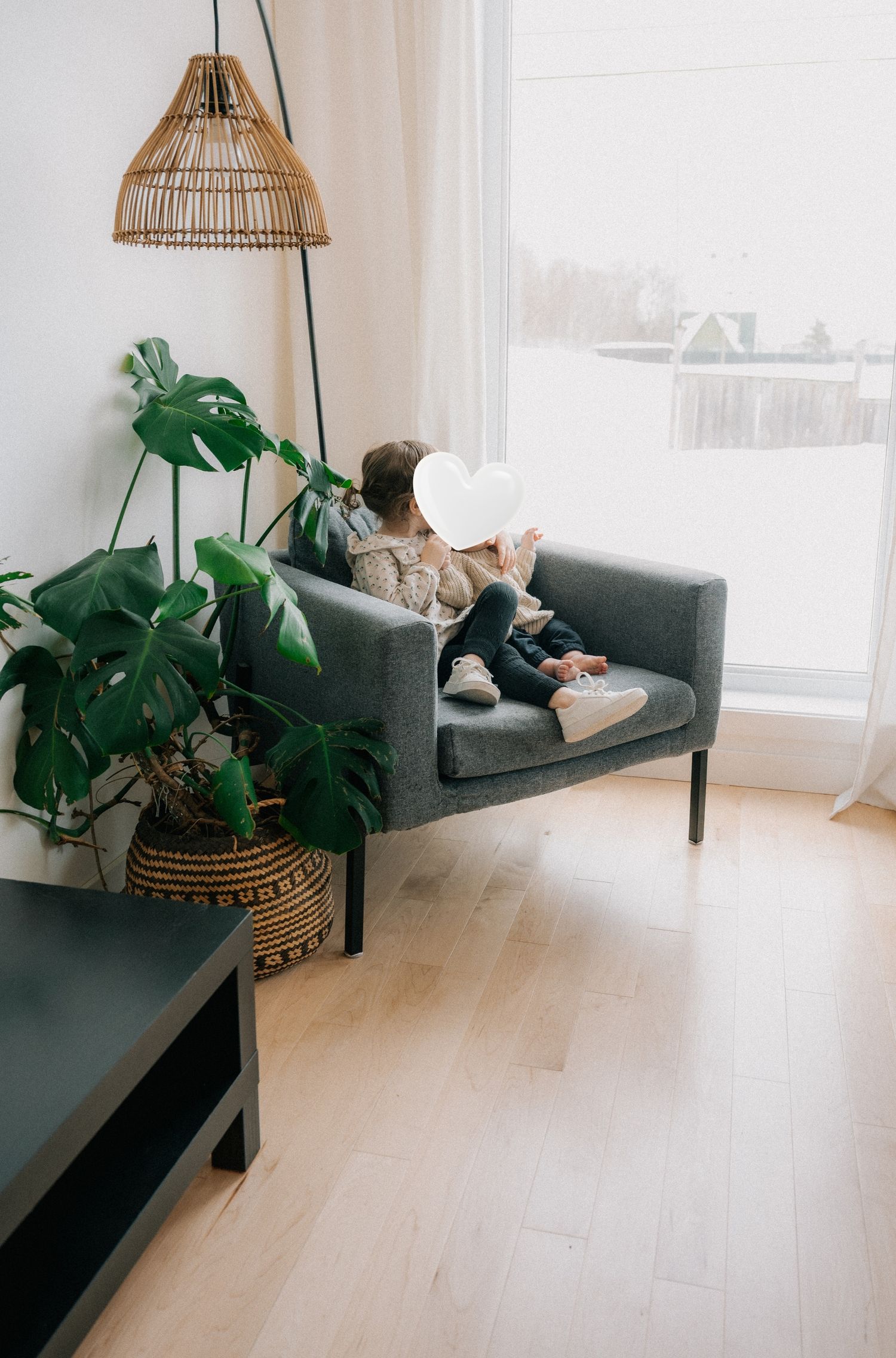 Person relaxing on a gray sofa beside a monstera plant and wicker pendant light in a bright Scandinavian living room.