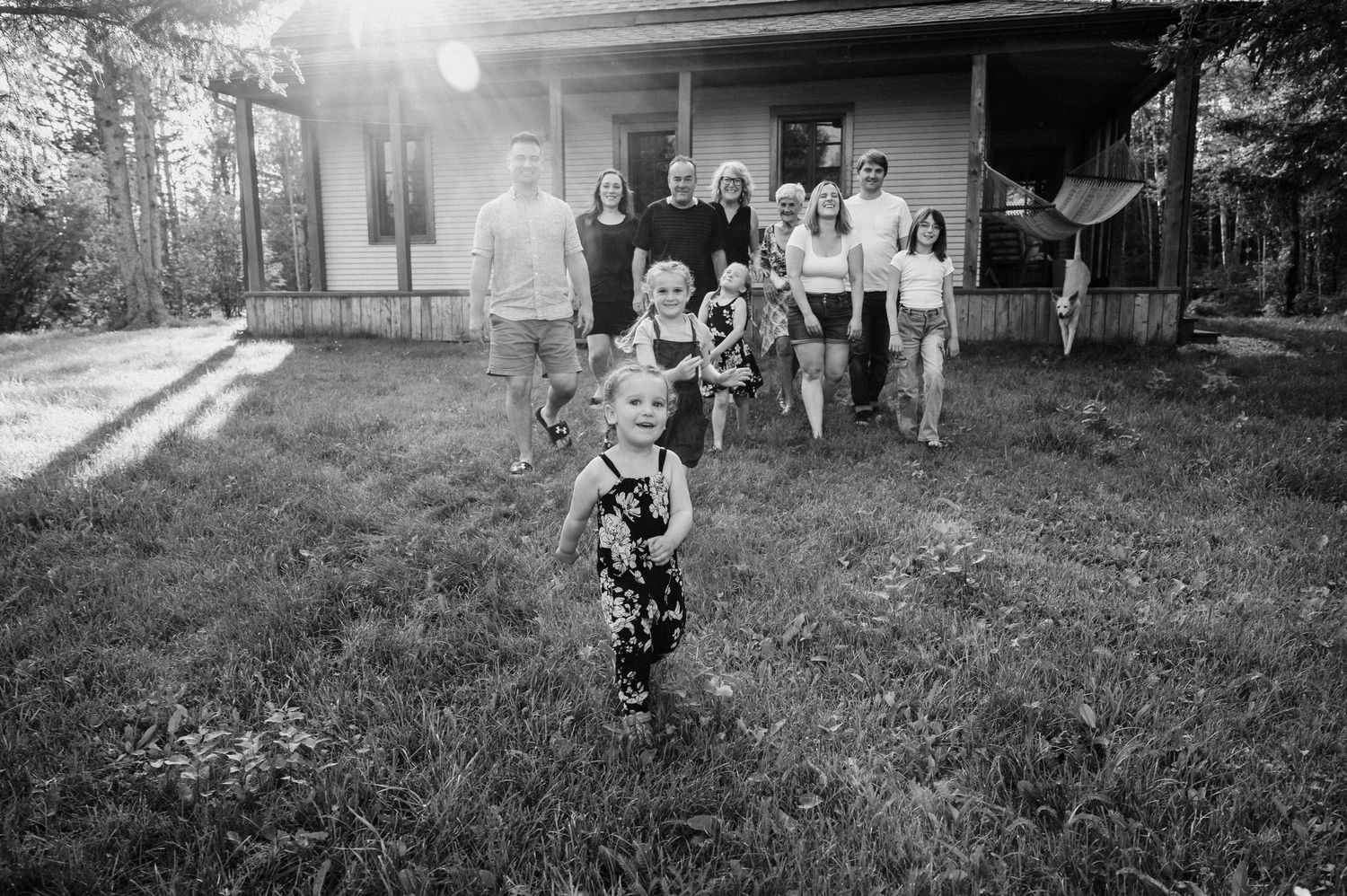 Photo de famille en noir et blanc prise devant une maison rustique avec des enfants jouant dans la cour.