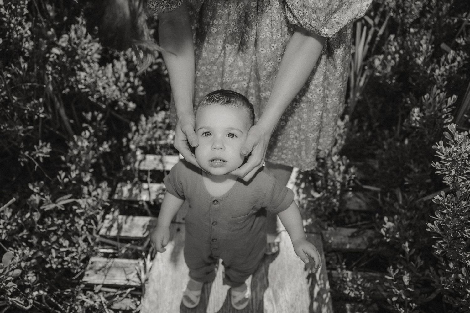 Une photographie en noir et blanc montre un petit enfant debout sur un vieux quai entouré de verdure.