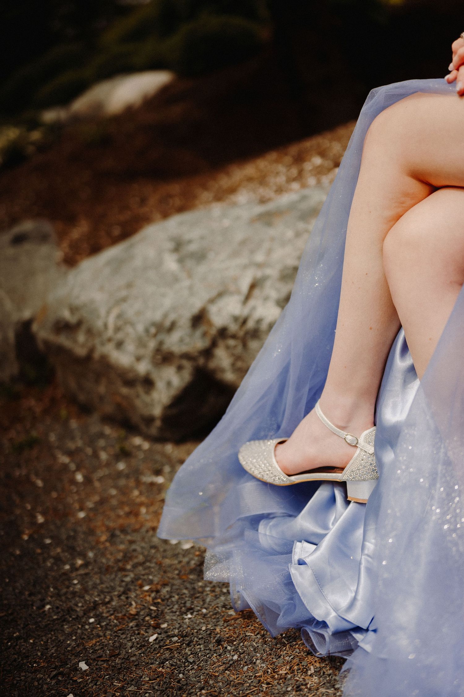 Elegant sparkly shoes peek out from beneath a flowing blue dress against rustic stone backdrop.