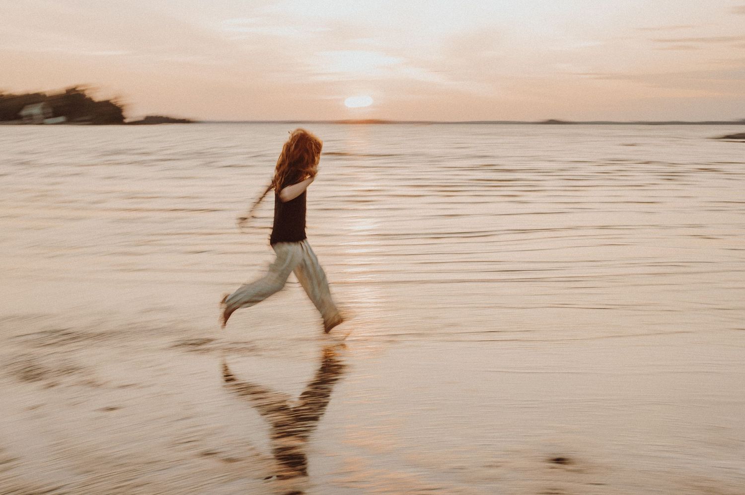 Un enfant court dans l’eau peu profonde au coucher du soleil, créant des reflets sur le sable mouillé.