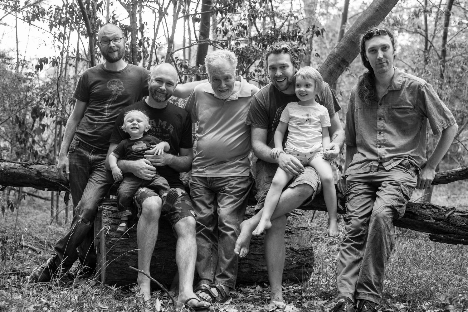 A family sits together on a fallen tree trunk in a black and white outdoor photo.