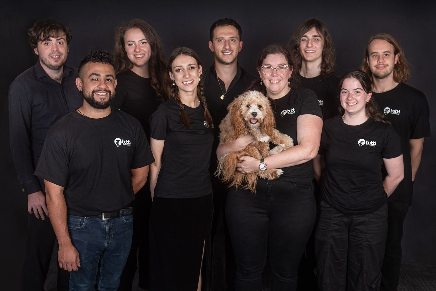 A group wearing matching black t-shirts poses together for a casual studio portrait with a dog.