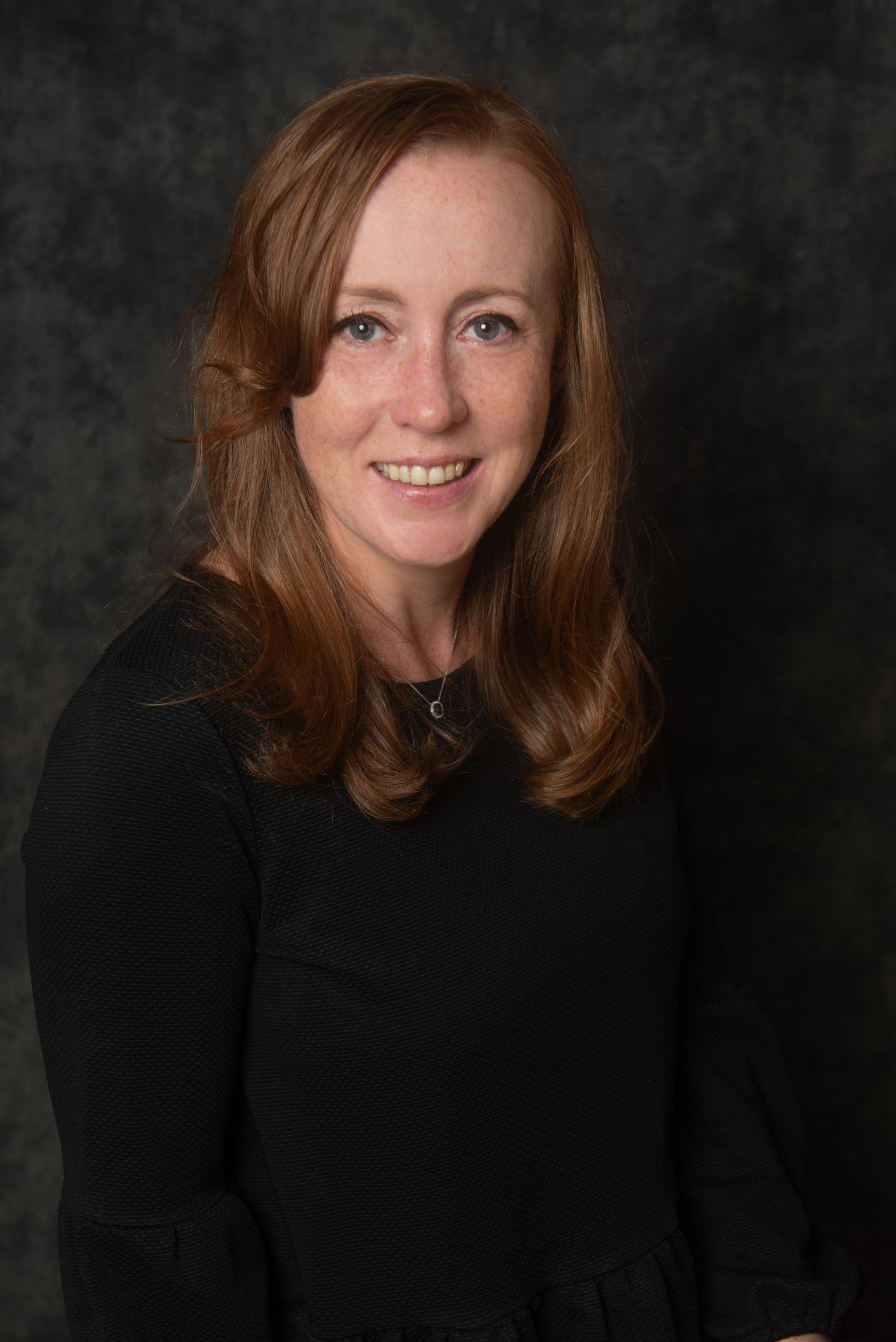 Professional headshot portrait against dark grey background.