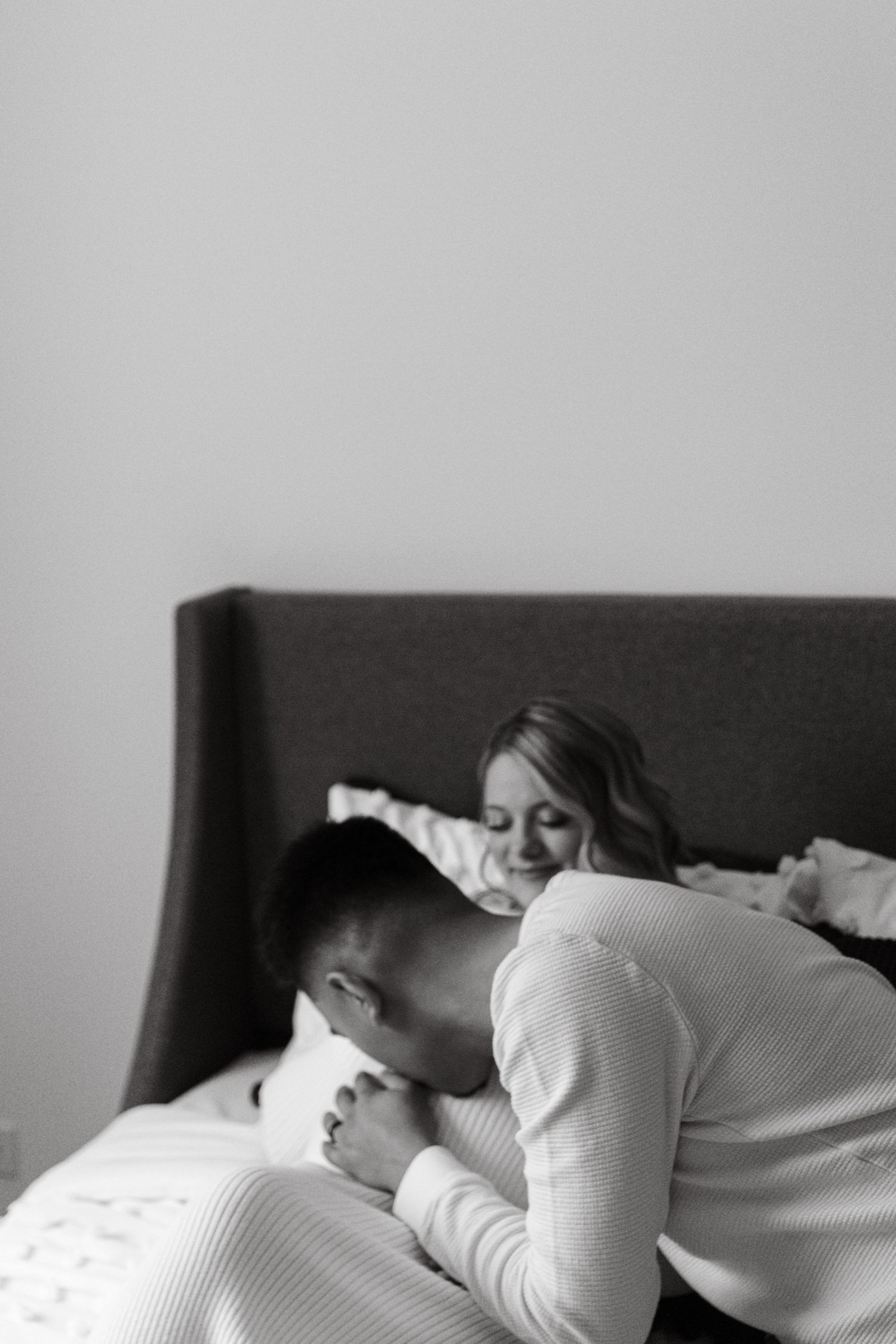 An expecting father kissing an expecting mother's baby bump while laying in bed,  captured by Box of Sunshine Studios