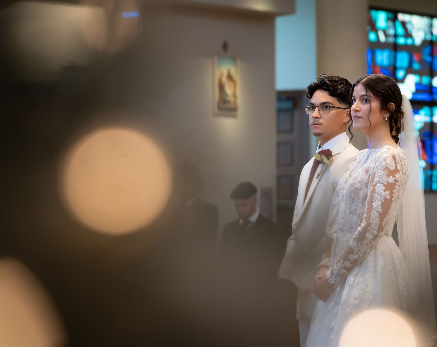 A couple stands together during a church wedding ceremony with beautiful stained glass windows in the background.