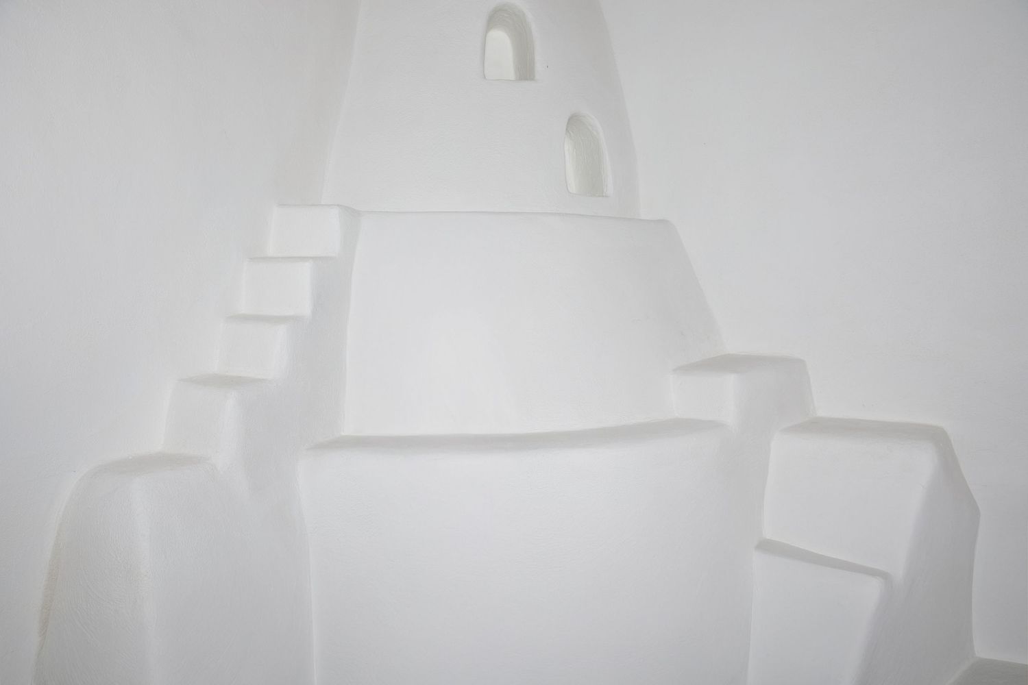 Abstract white sculptural installation with stacked geometric forms creating a castle-like structure against a white background.