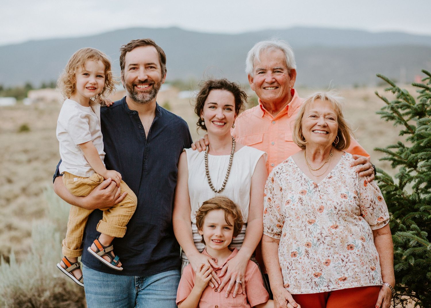 Multi-generational family portrait outdoors with mountains and desert landscape in background.