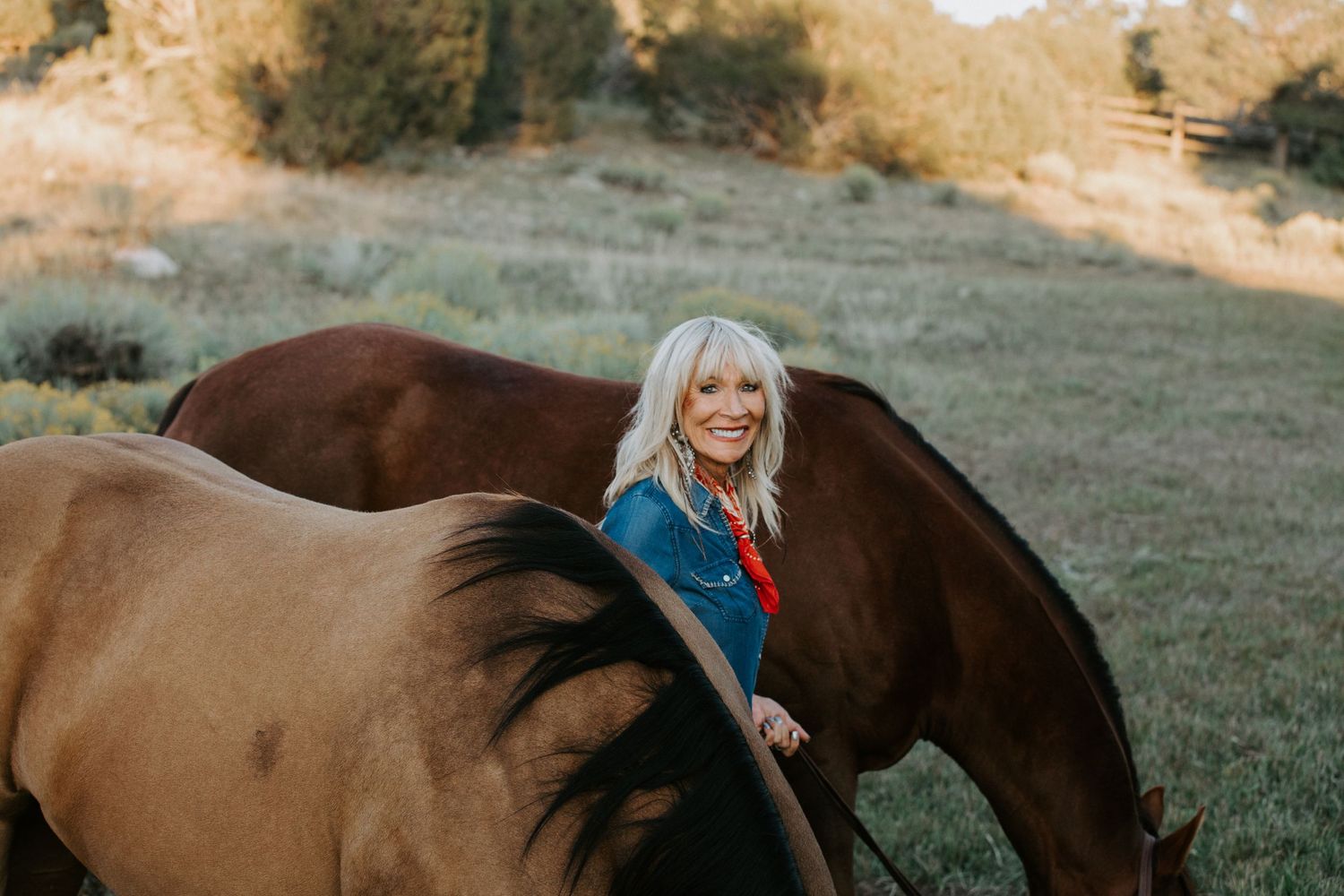 Western lifestyle portrait in Taos NM with woman in denim standing beside a horse in a scenic outdoor setting